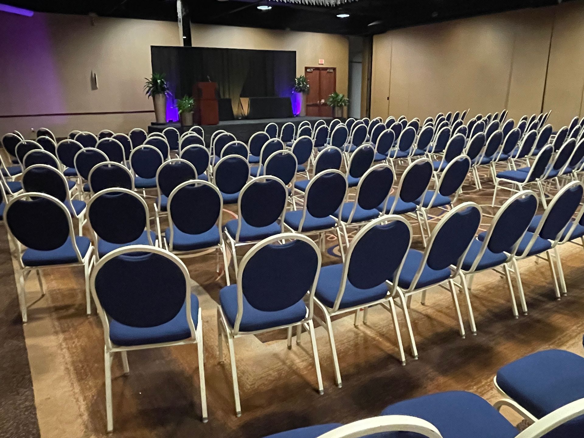 Rows of blue chairs in a conference room with a stage in the background.