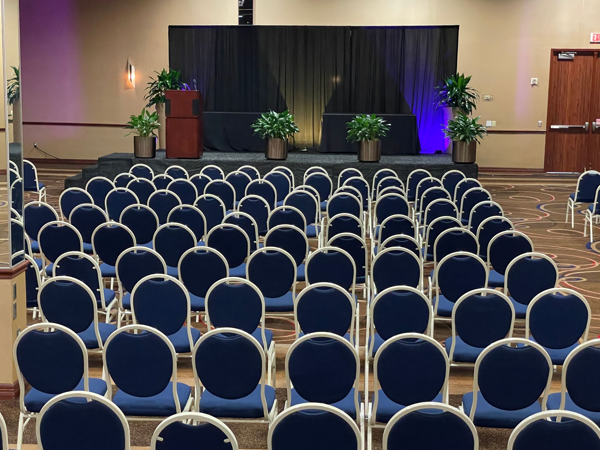Rows of blue chairs in a room with a stage in the background
