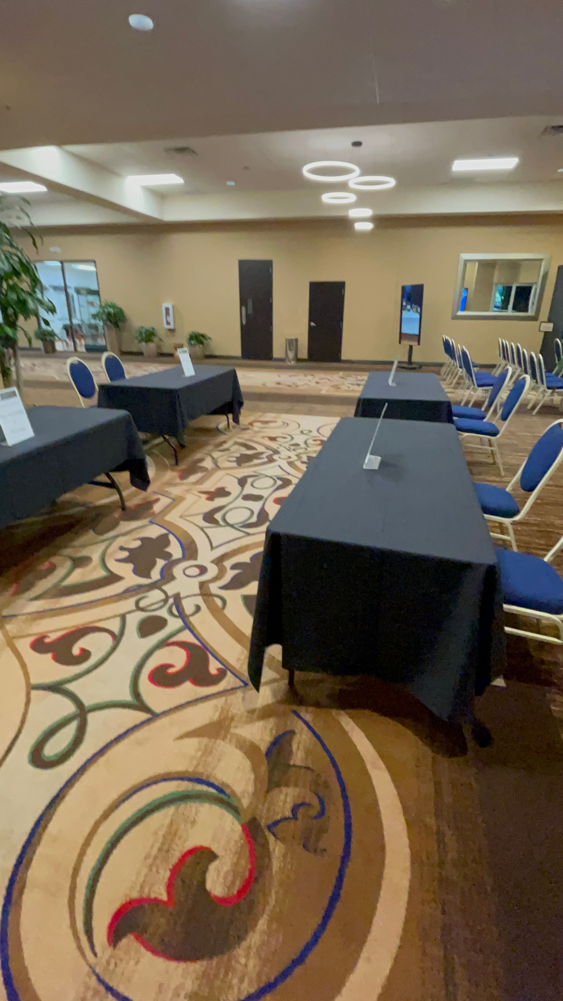 A ballroom with black-covered tables, blue chairs, and patterned carpet.