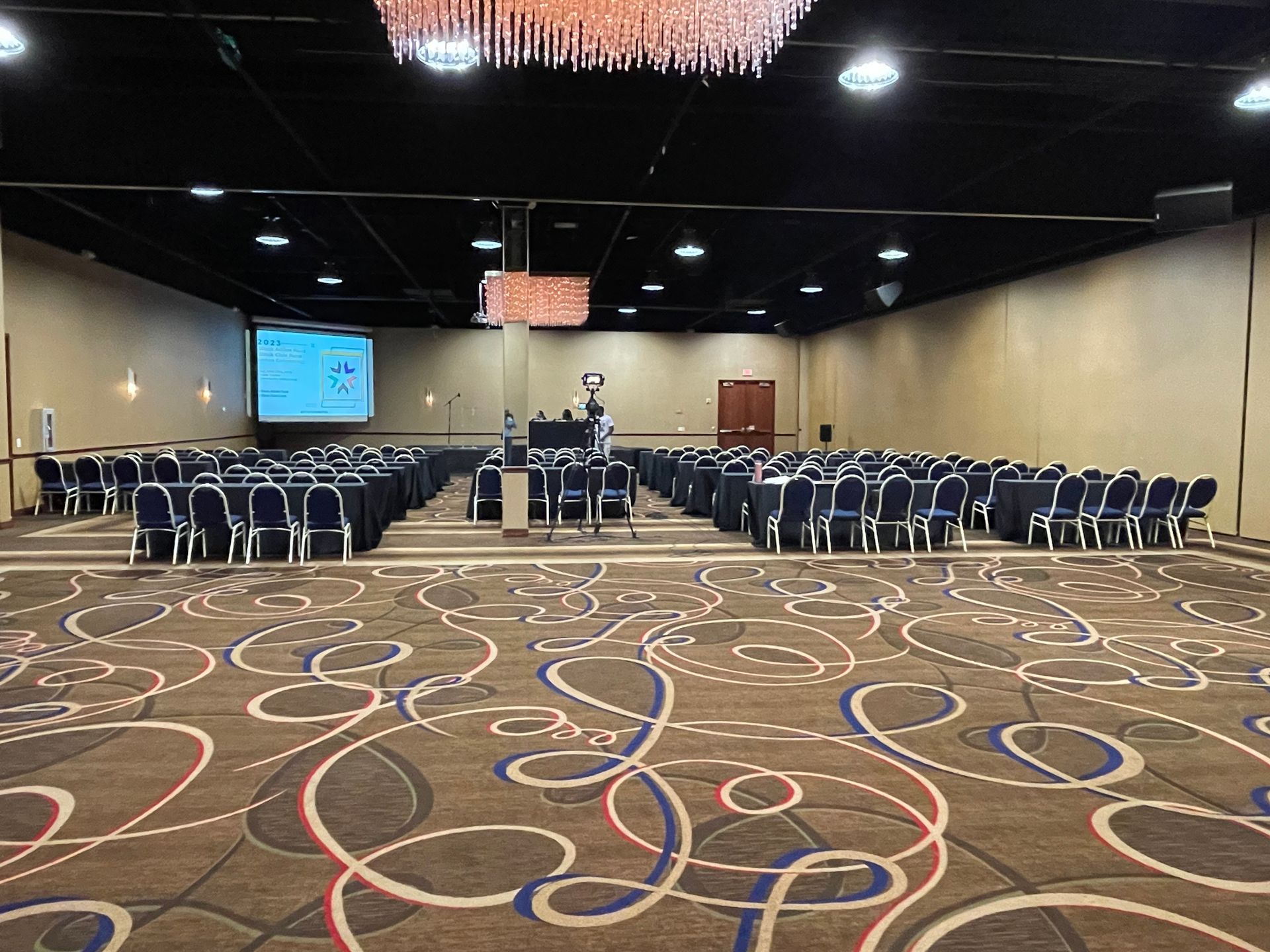 A large conference room with tables and chairs and a projector screen.