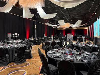 Elegant banquet hall with black table settings, chandeliers, and draped white ceiling fabric