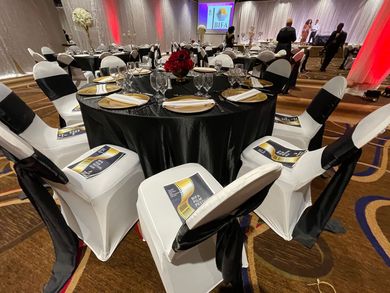 Round banquet tables with black tablecloths and white chair covers in a decorated event hall