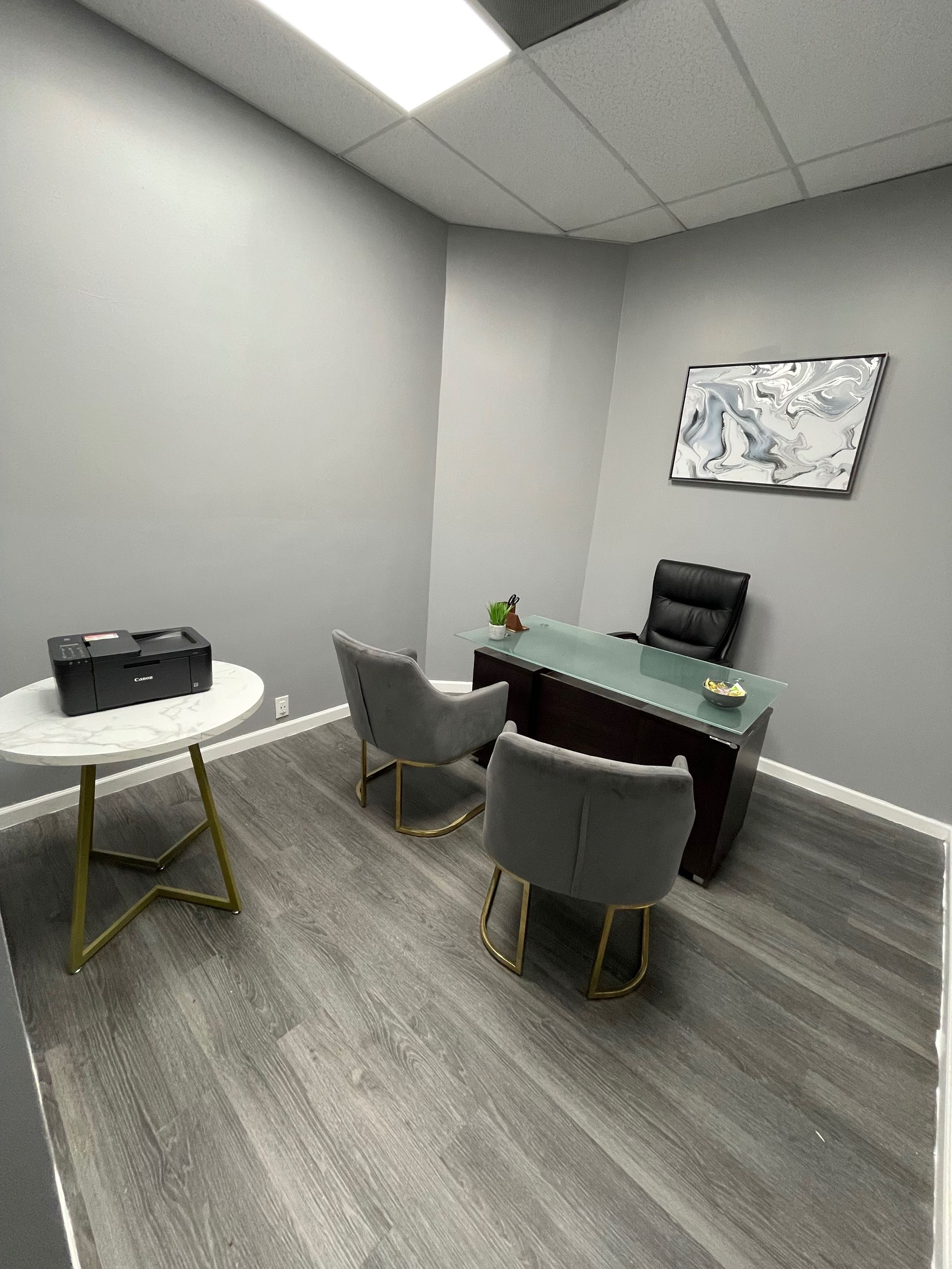 Office space with a desk, chairs, and a round table. Gray walls and flooring.