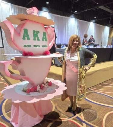 A woman is standing in front of a giant teapot with green letters on it.