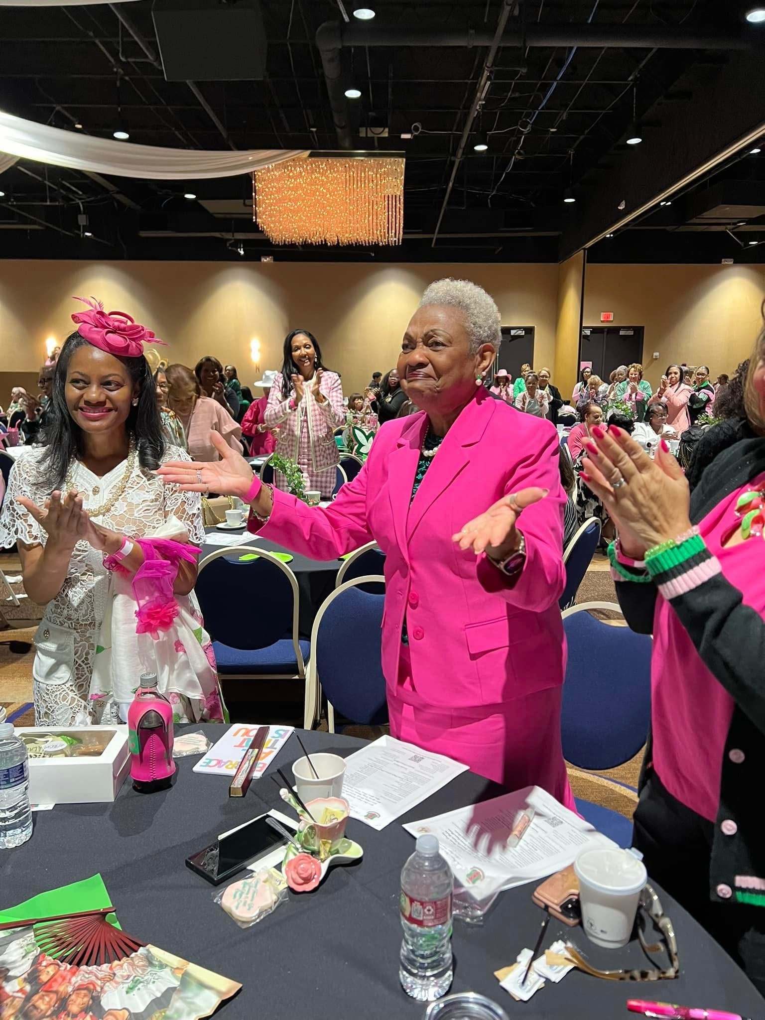A group of women are sitting at a table in a room clapping their hands.
