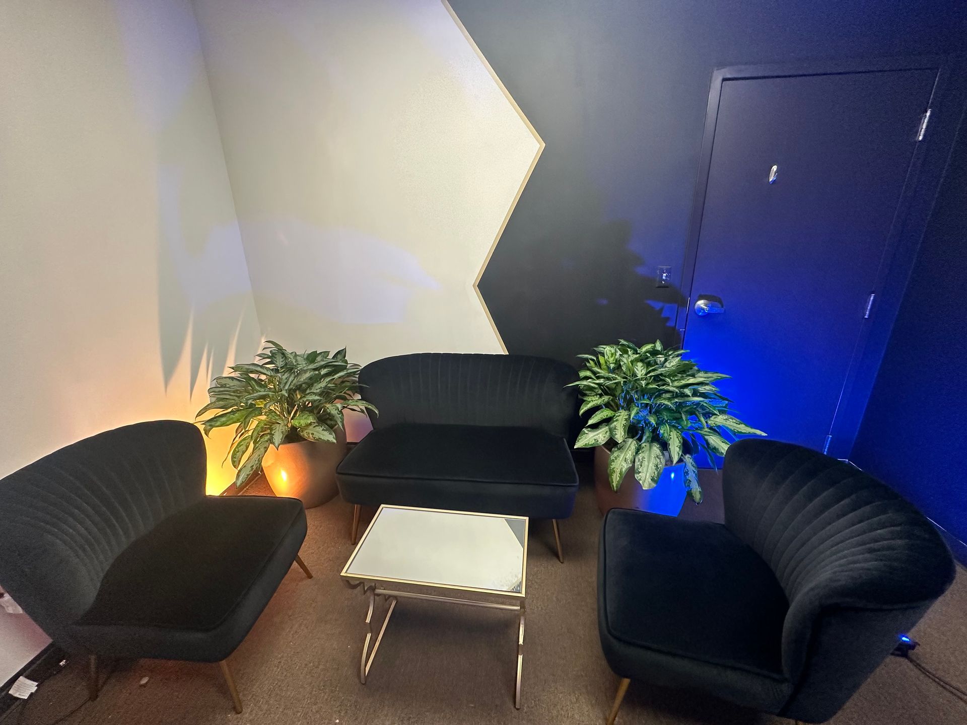 A living room with black chairs , a couch , a table and a plant.