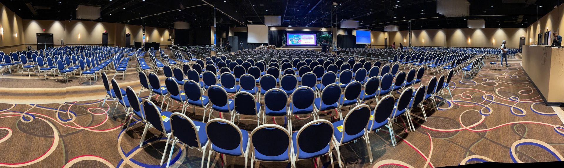 A large conference room filled with blue chairs and a stage.