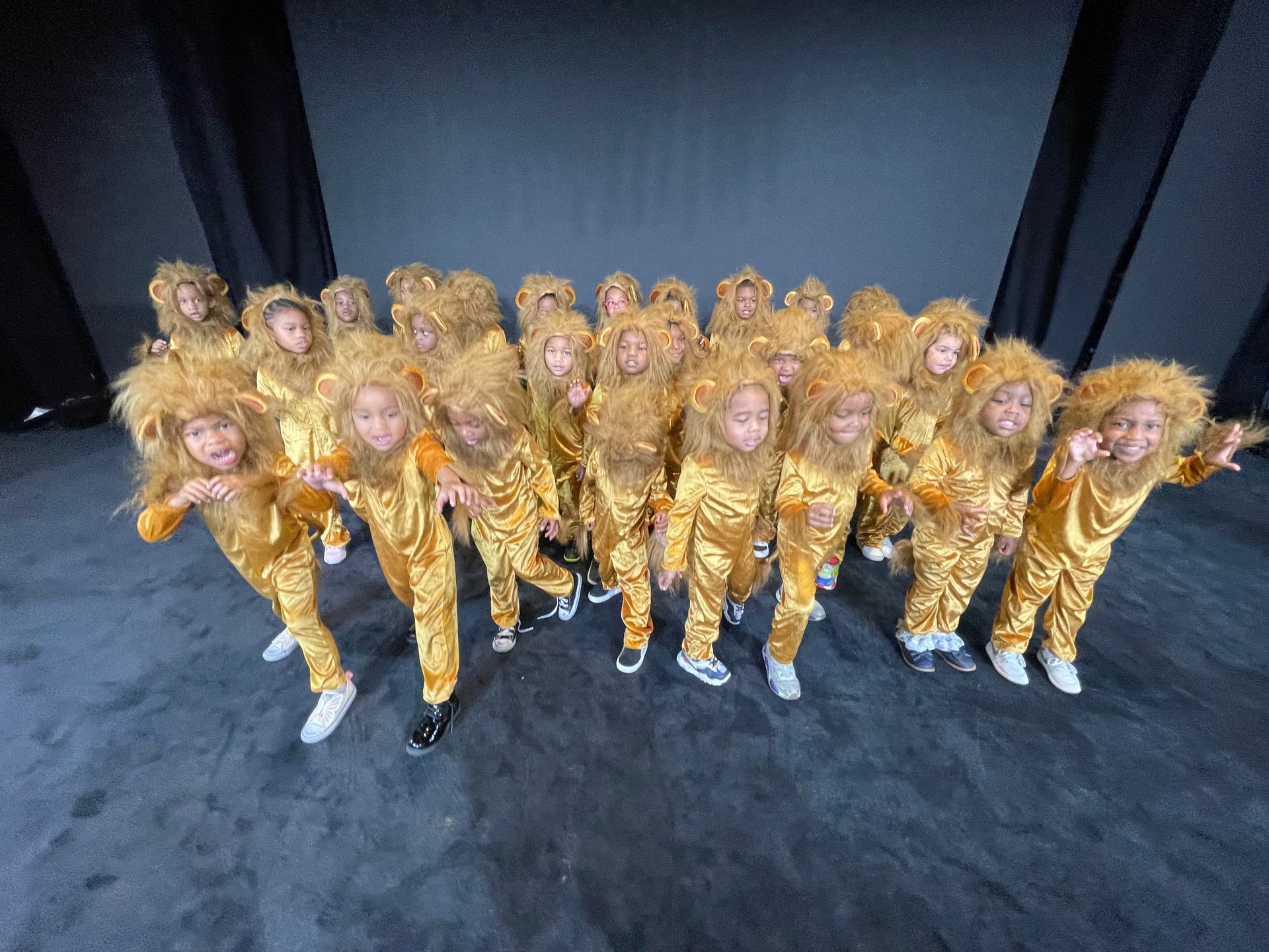 A group of children dressed in lion costumes are posing for a picture on a stage.