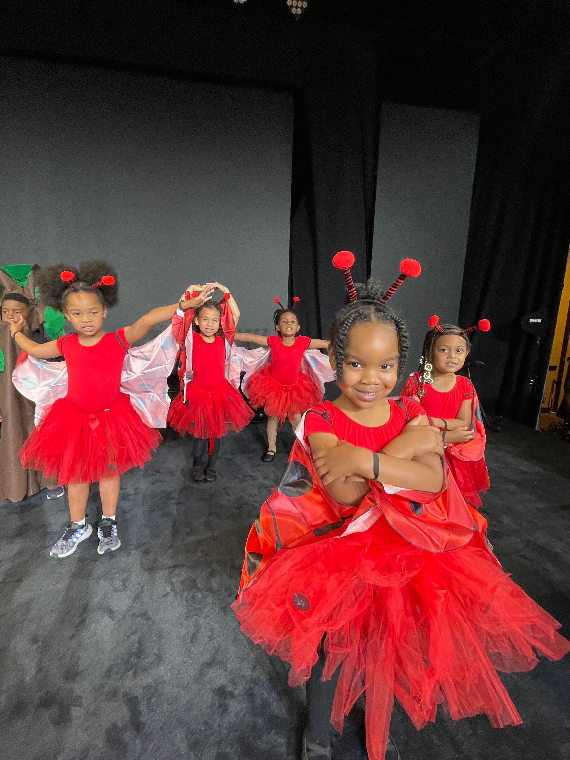 A group of little girls dressed in red ladybugs costumes are dancing on a stage.