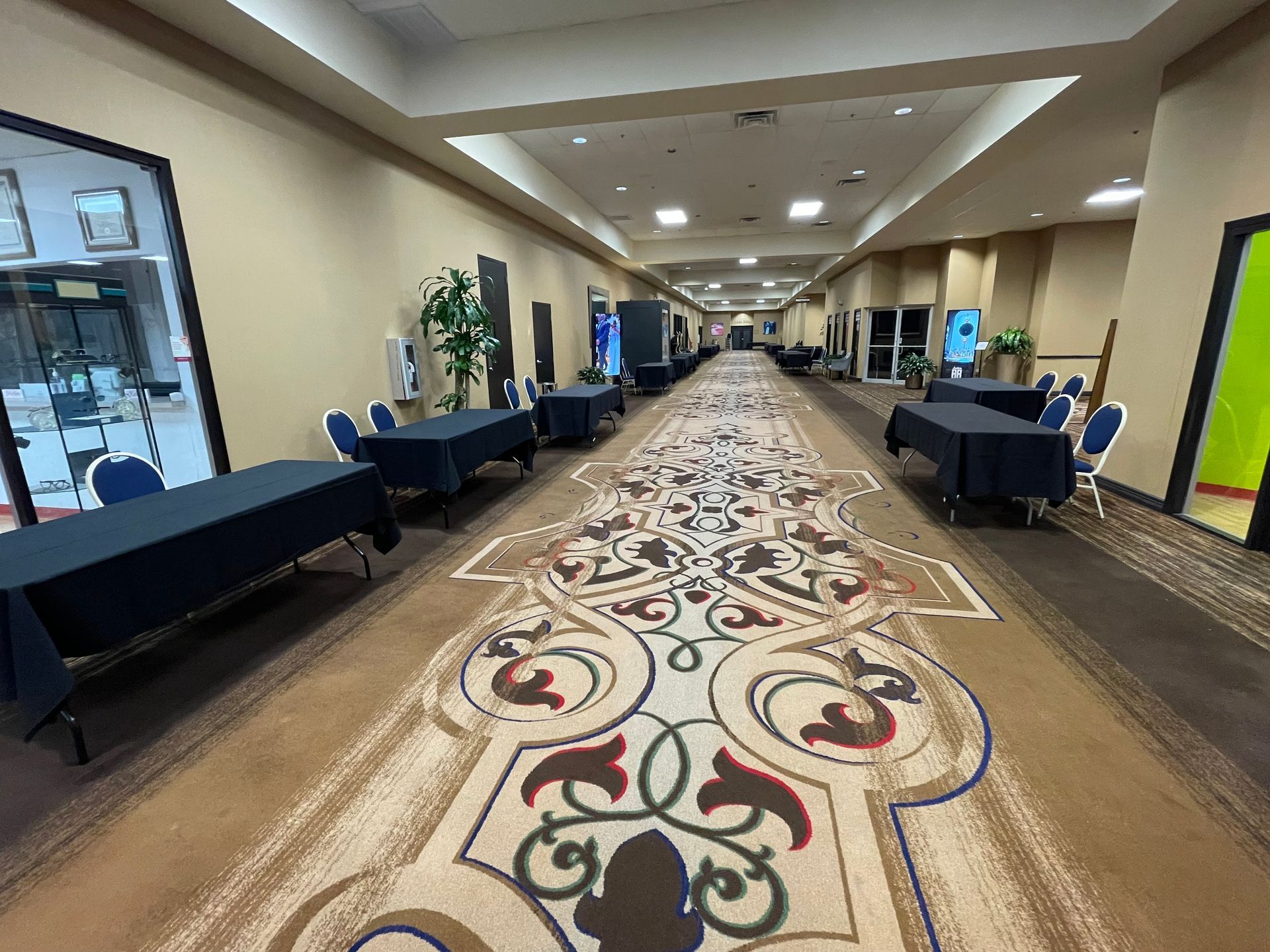 Long hallway with a decorative carpet, tables with black tablecloths, and doorways.