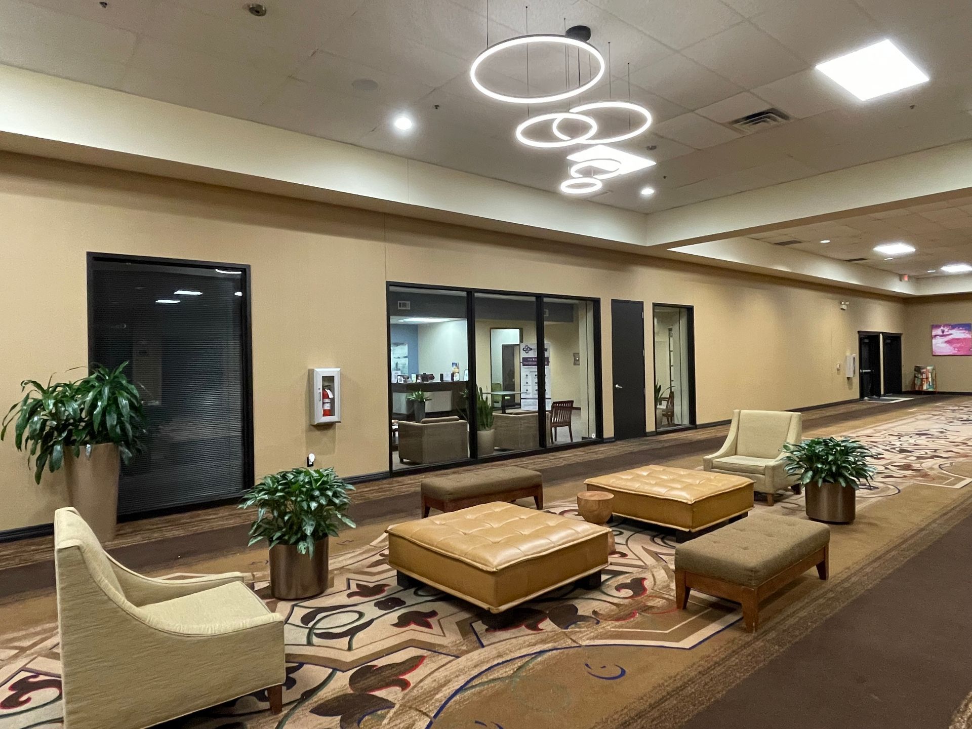 Lobby with tan walls, brown carpet, seating areas, plants, and modern circular light fixtures.