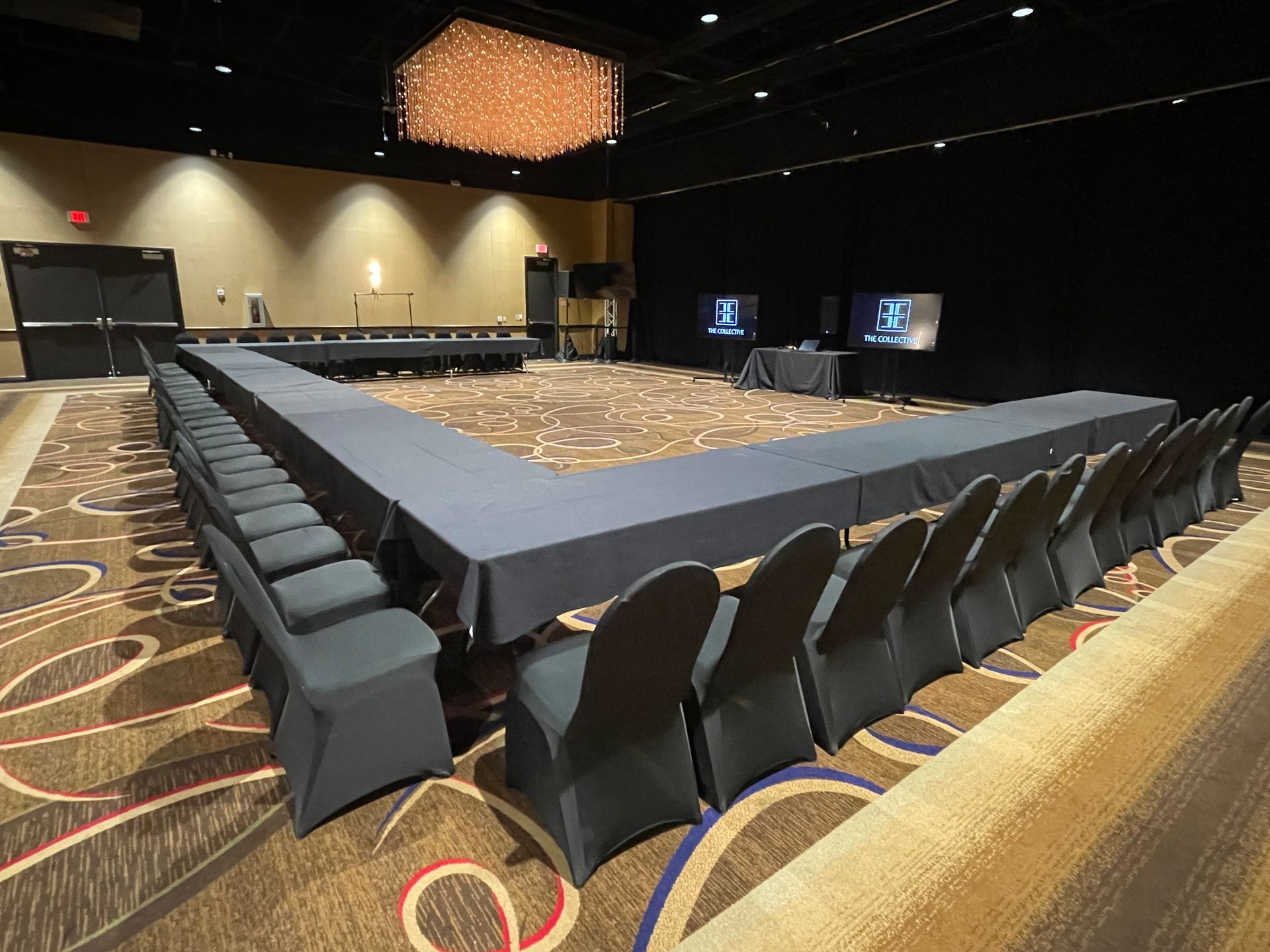 Conference room set up in a U-shape with dark blue tables and chairs on patterned carpet.