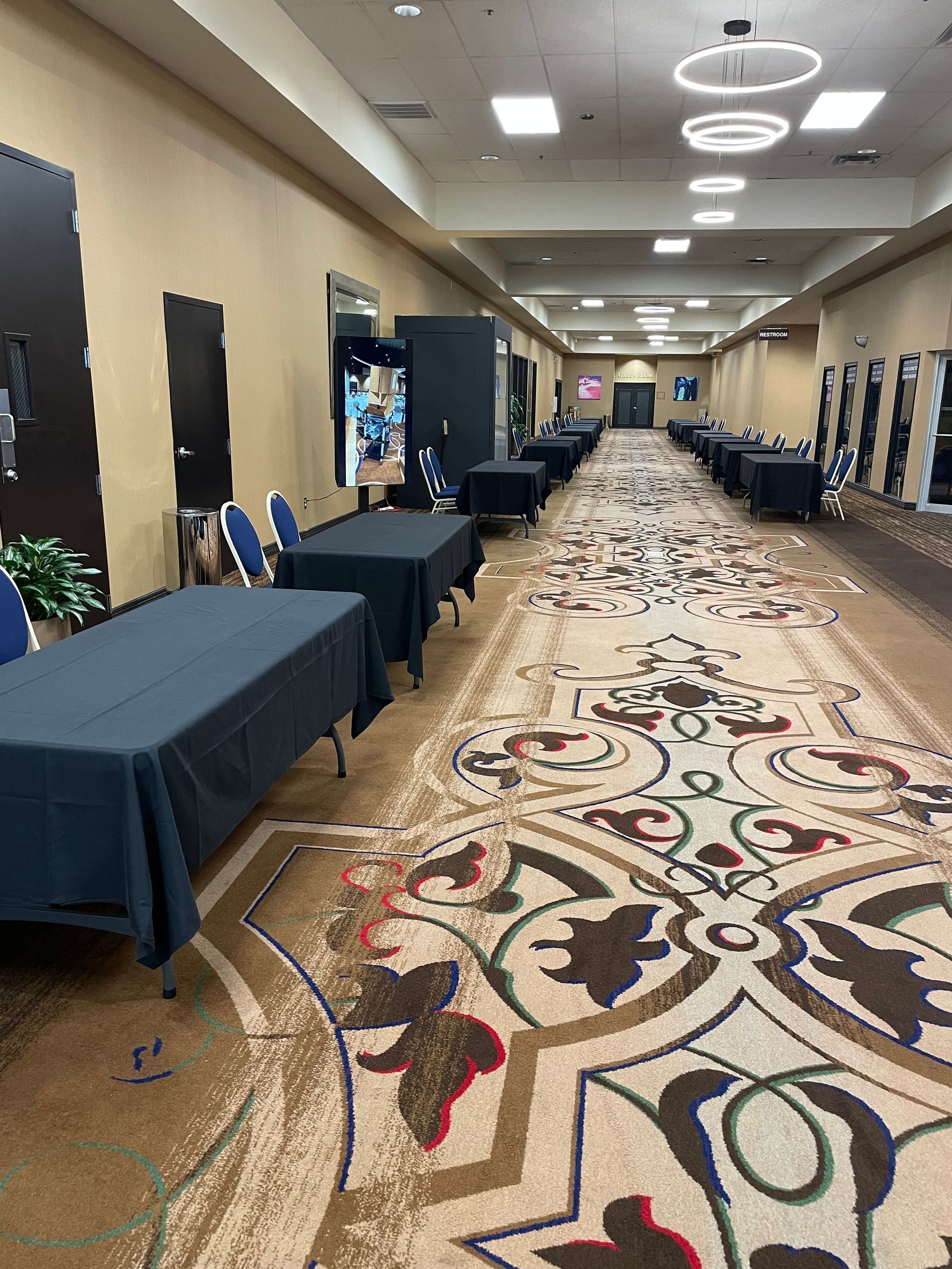 Long hallway with tables covered in black cloth, ornate carpet, overhead lights.