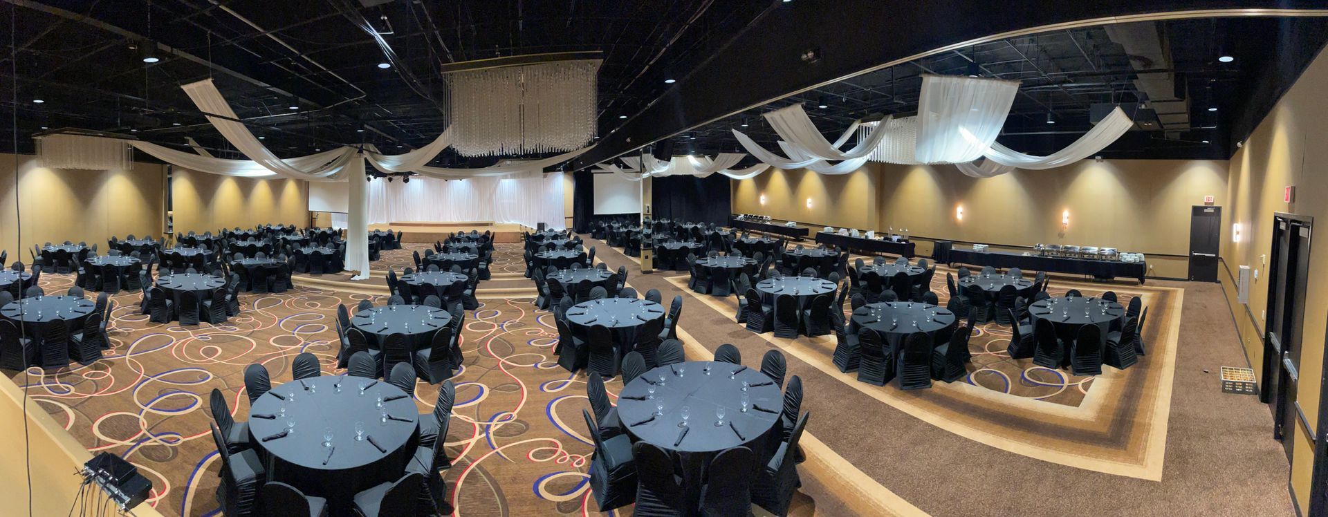 A large banquet hall with round tables covered in black cloth set for an event.