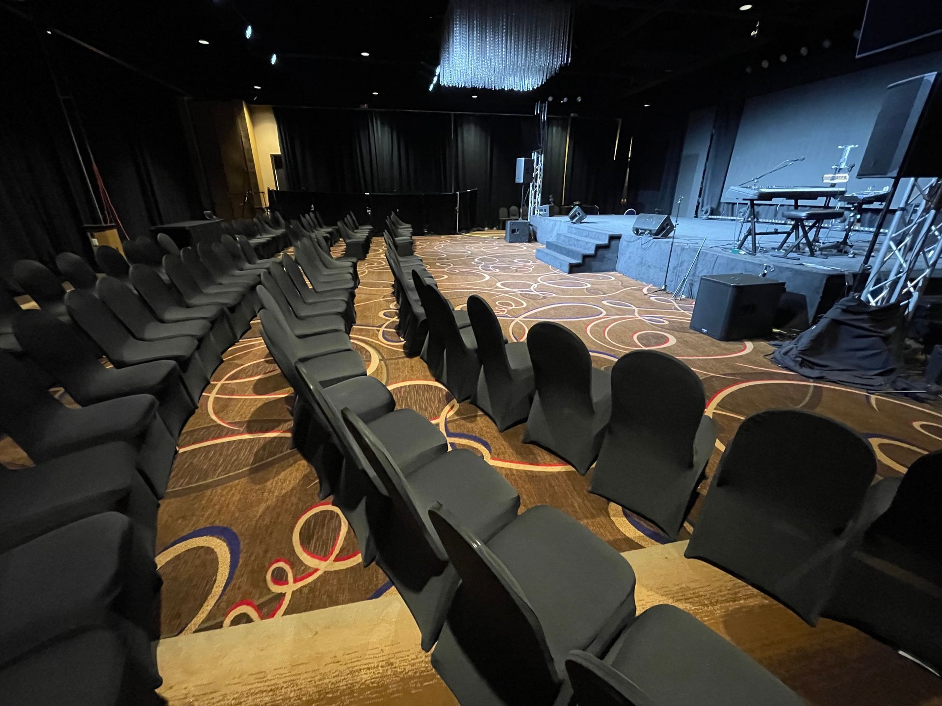 Rows of black chairs face a stage in a dark event space.