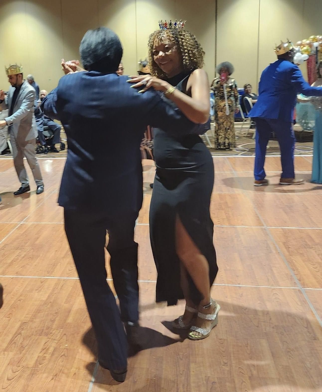 A woman in a black dress is dancing with a man in a blue suit