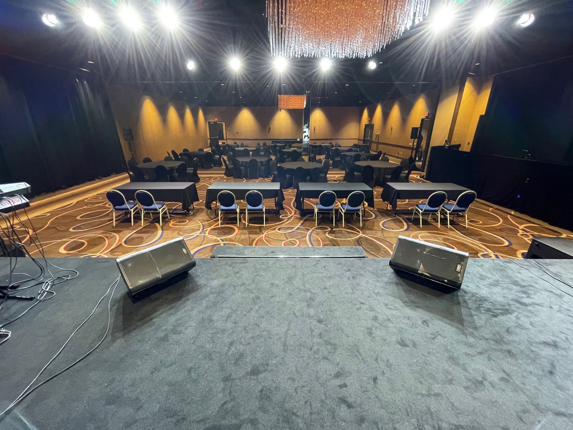 A large room with tables and chairs and speakers on the stage.