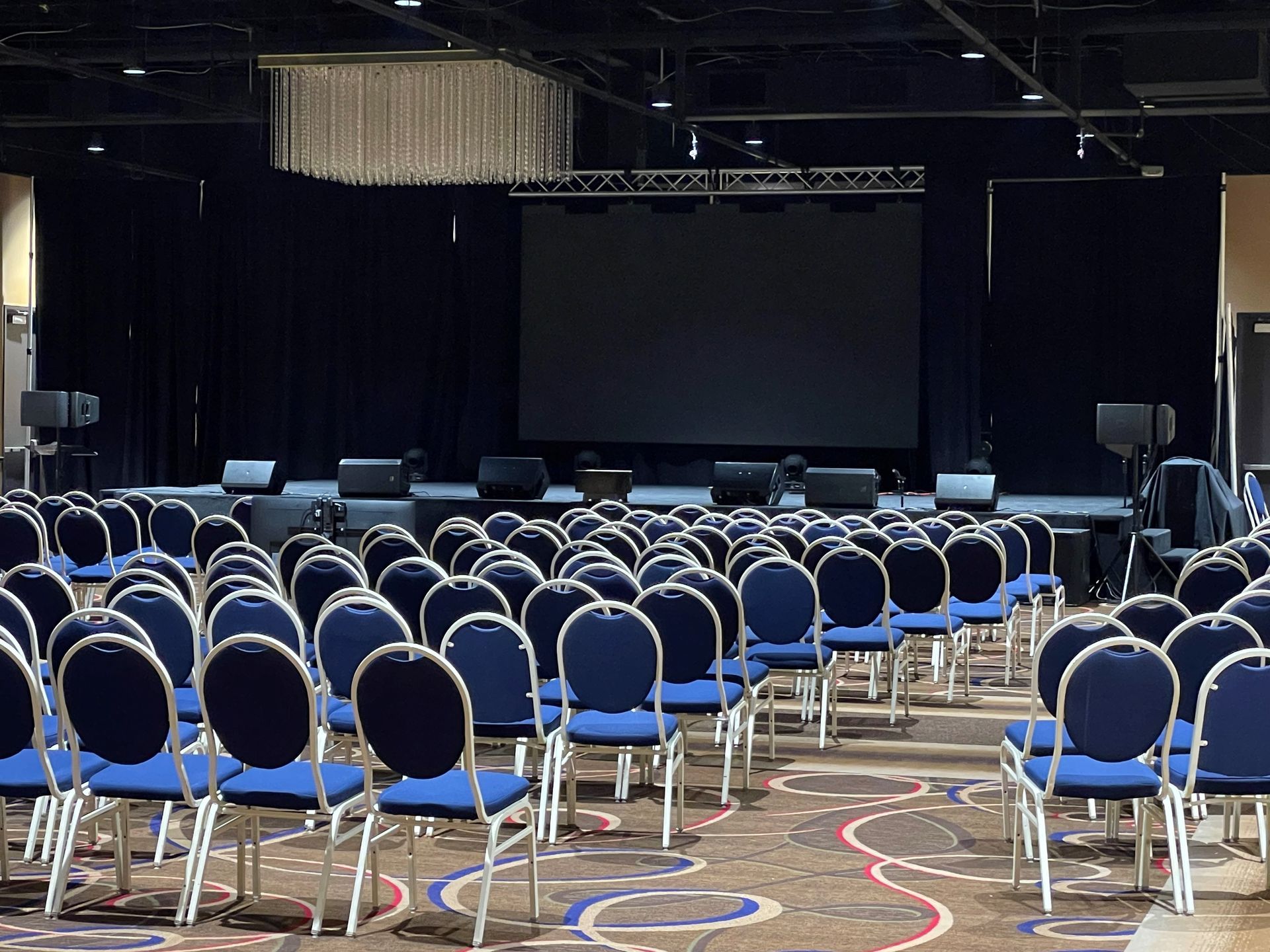 Rows of blue chairs are lined up in front of a large screen in a conference room.