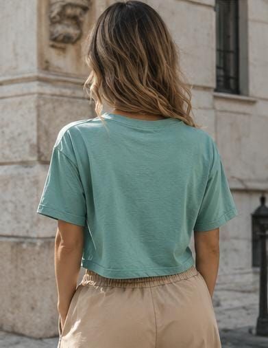 Persona vista de espaldas con una camiseta corta verde menta y pantalones beige en una calle de la ciudad.