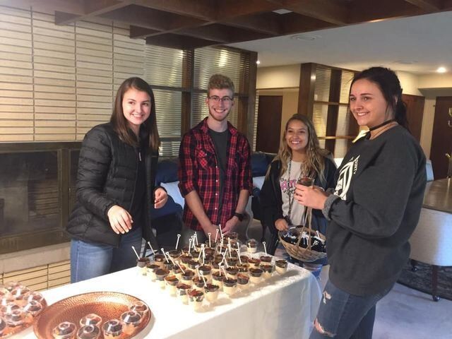 A group of people are standing around a table with cupcakes on it.