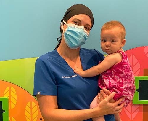 A woman wearing a mask is holding a baby in her arms.