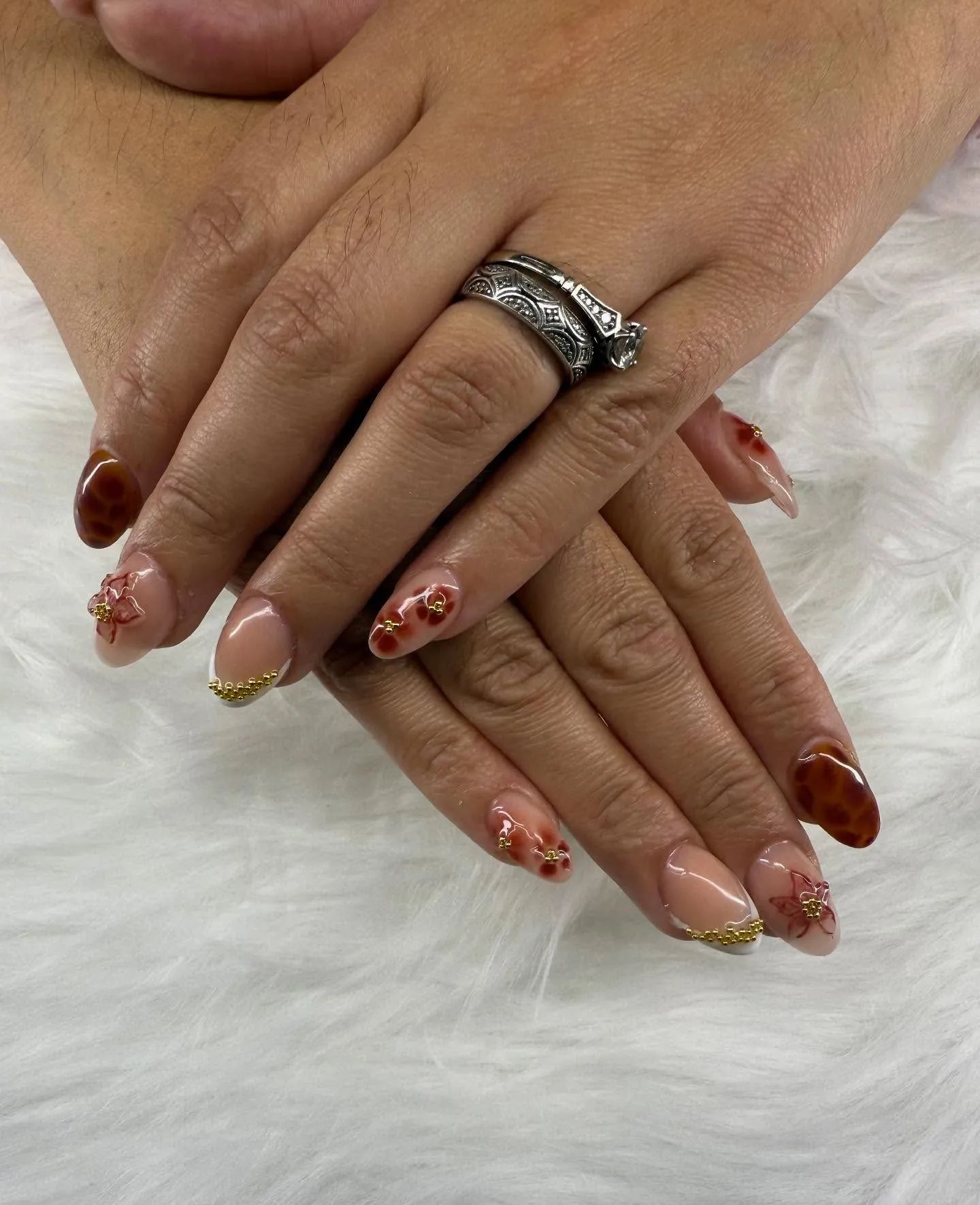 Hands with red and nude floral nail art, one wearing a silver ring, resting on white fur.