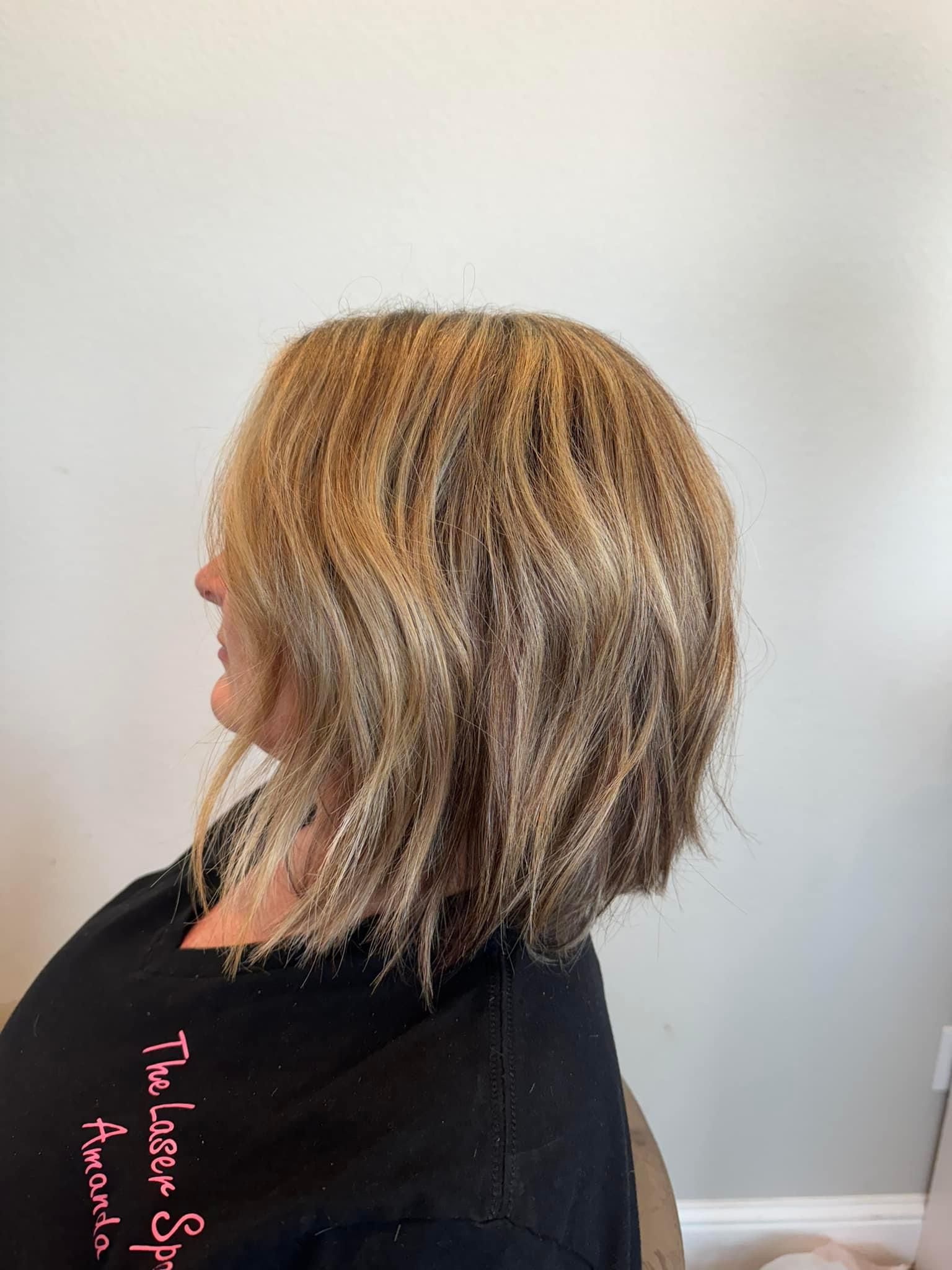 Woman with layered, crimped, blonde and brown hair. Wearing a black top in a salon setting.