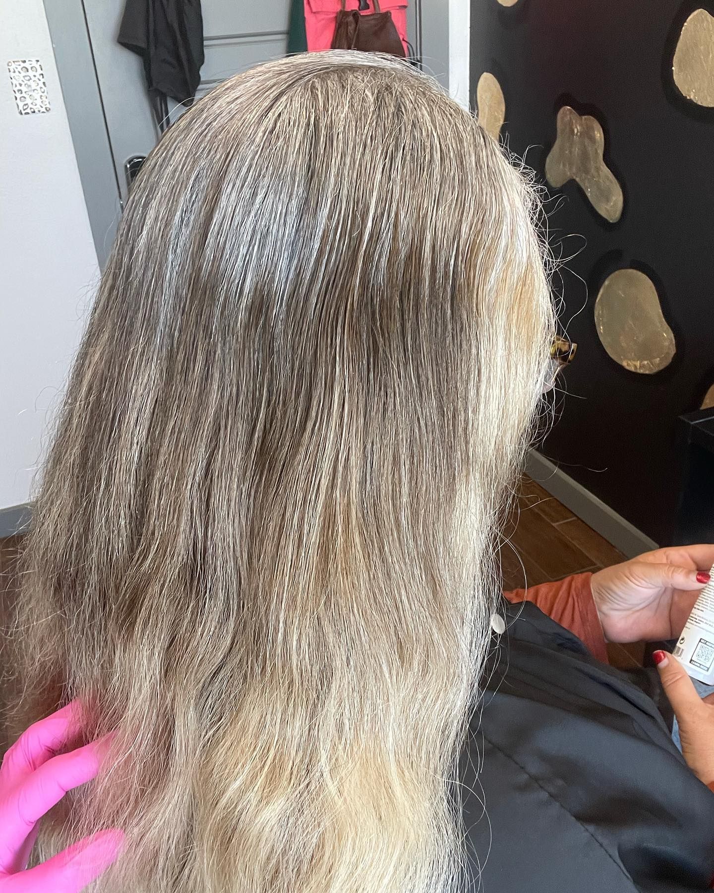 Hair with blonde dye being applied in a salon. Pink gloved hand and a white bottle are visible.