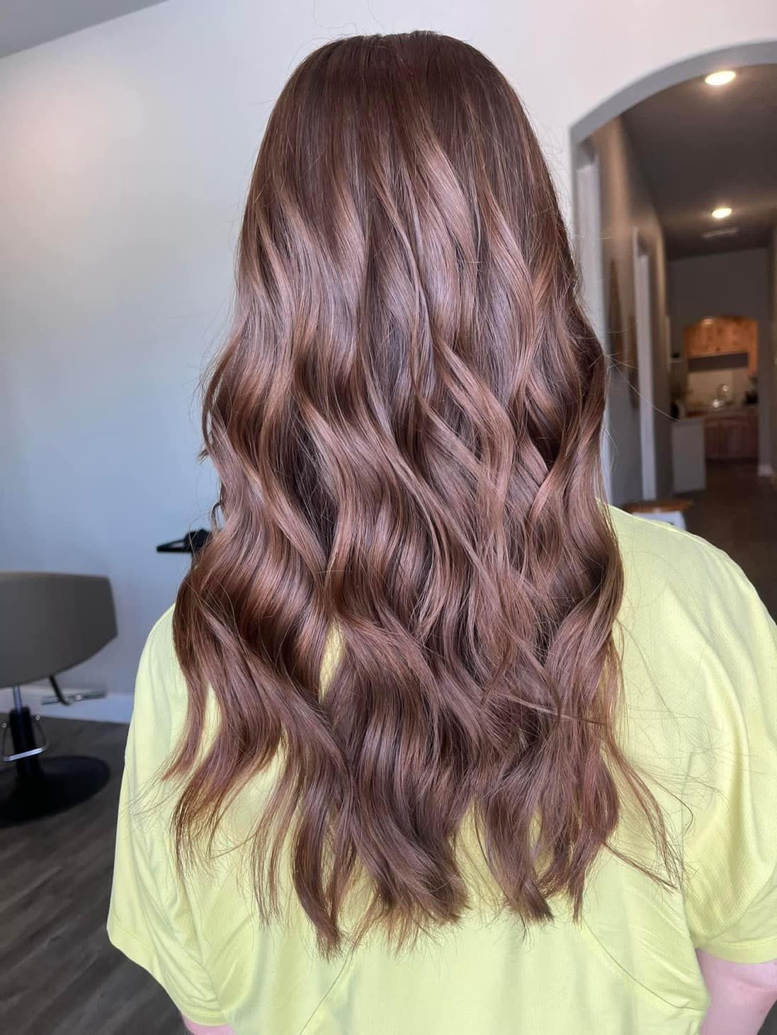 Woman with long, wavy brown hair. Wearing a yellow shirt in a salon setting.