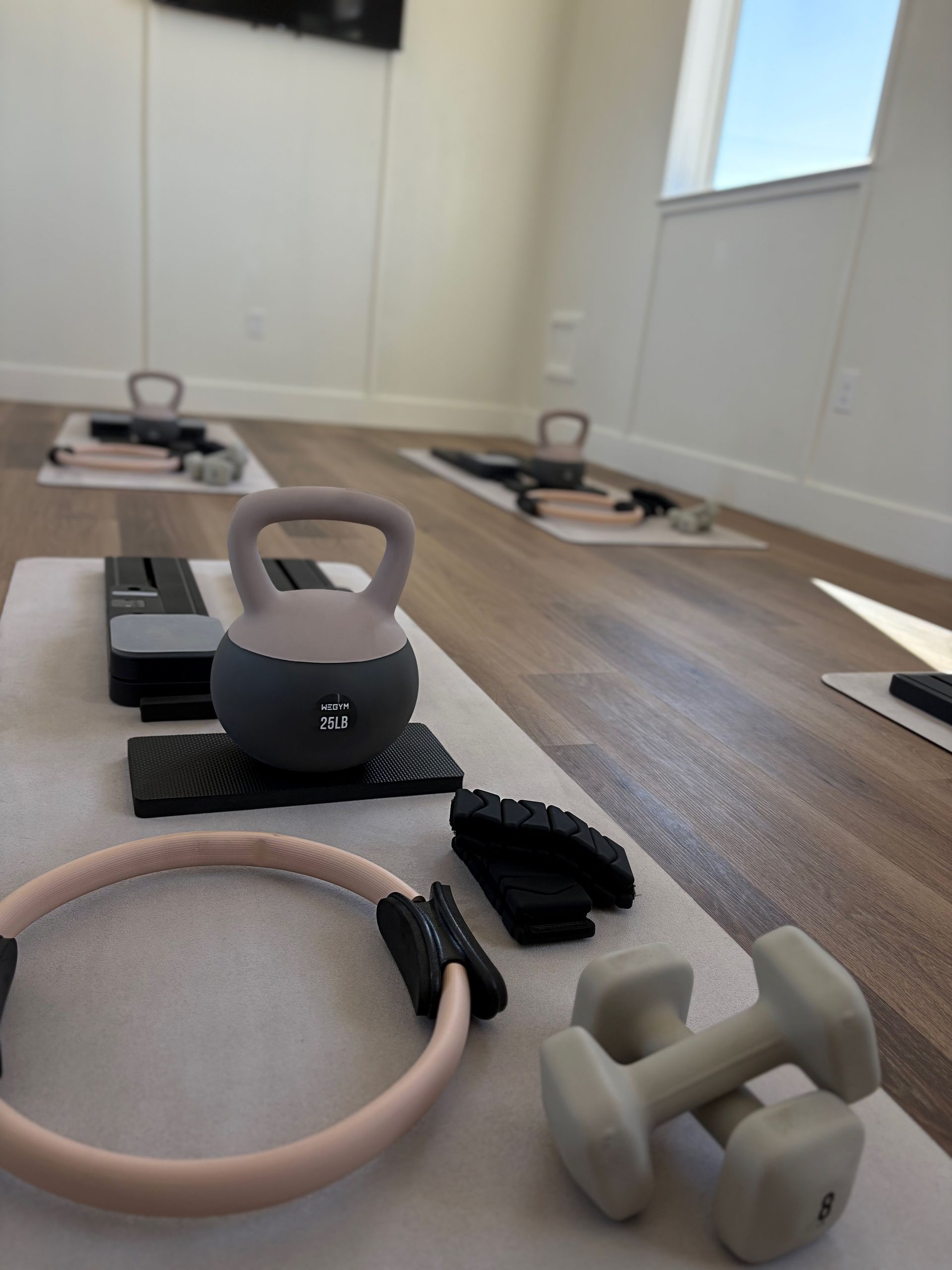 Fitness equipment on white mats in a workout room: kettlebell, dumbbells, Pilates ring.