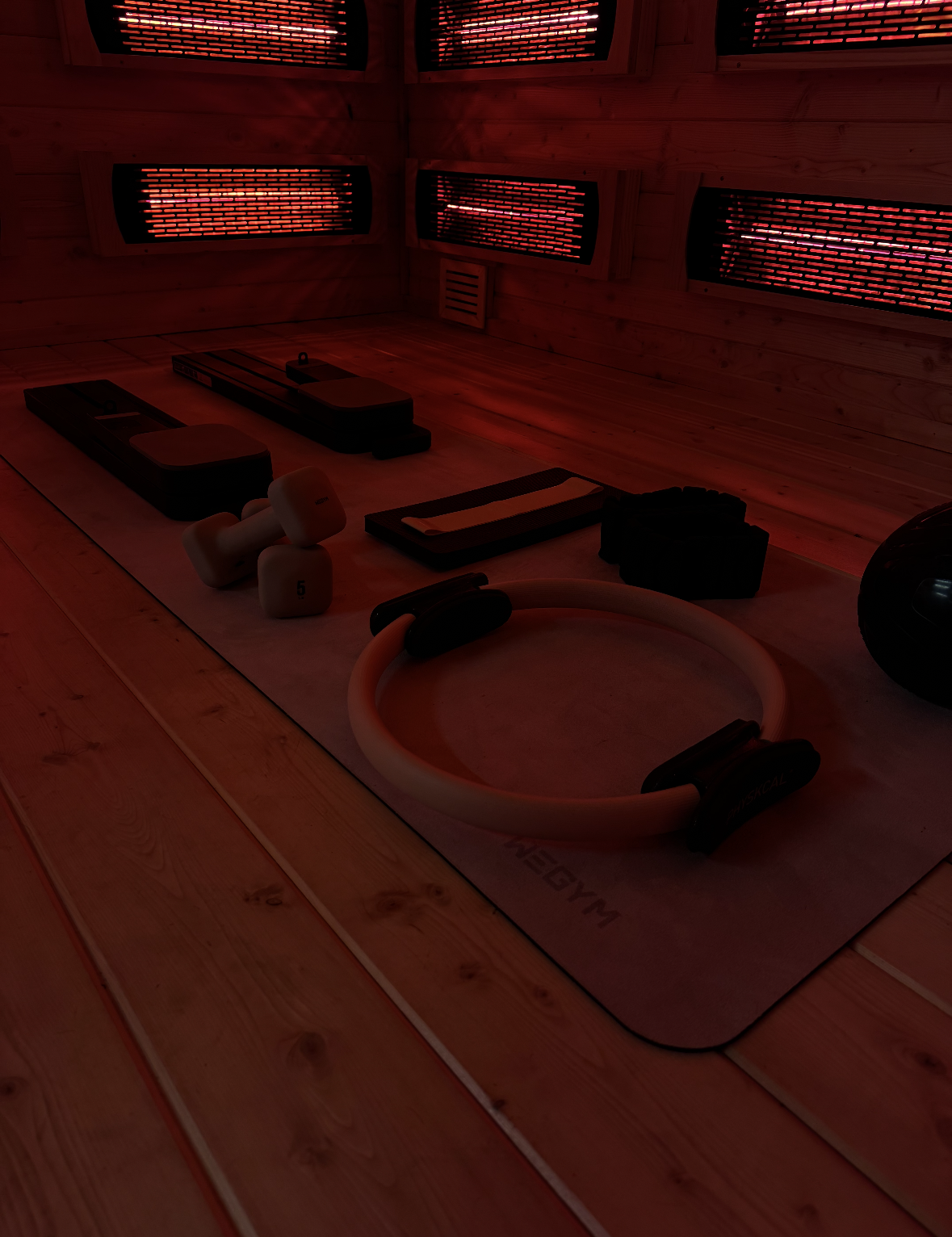 Infrared sauna interior with workout equipment on a mat; red glow from heating panels.