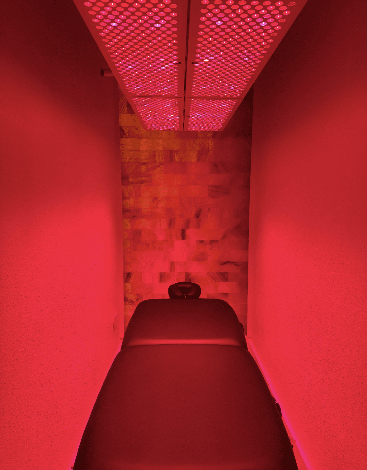 Red light therapy bed, red glow illuminates room, overhead panel.