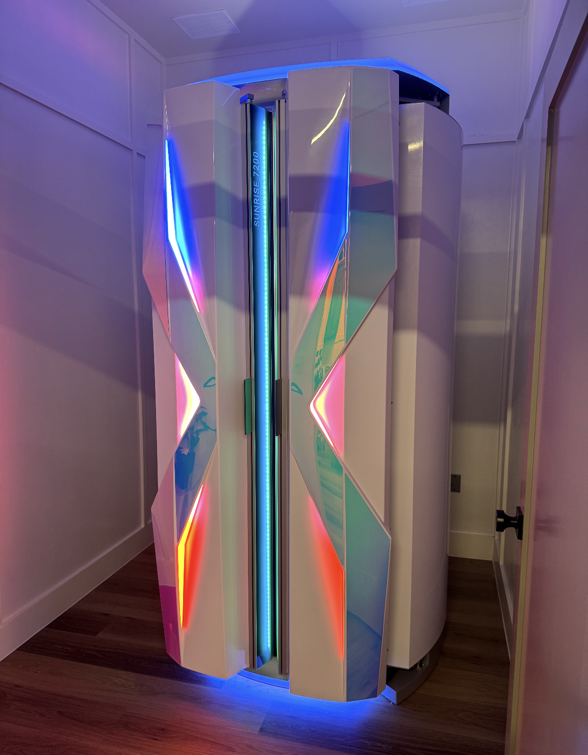 White tanning bed with blue and pink lights in a room.