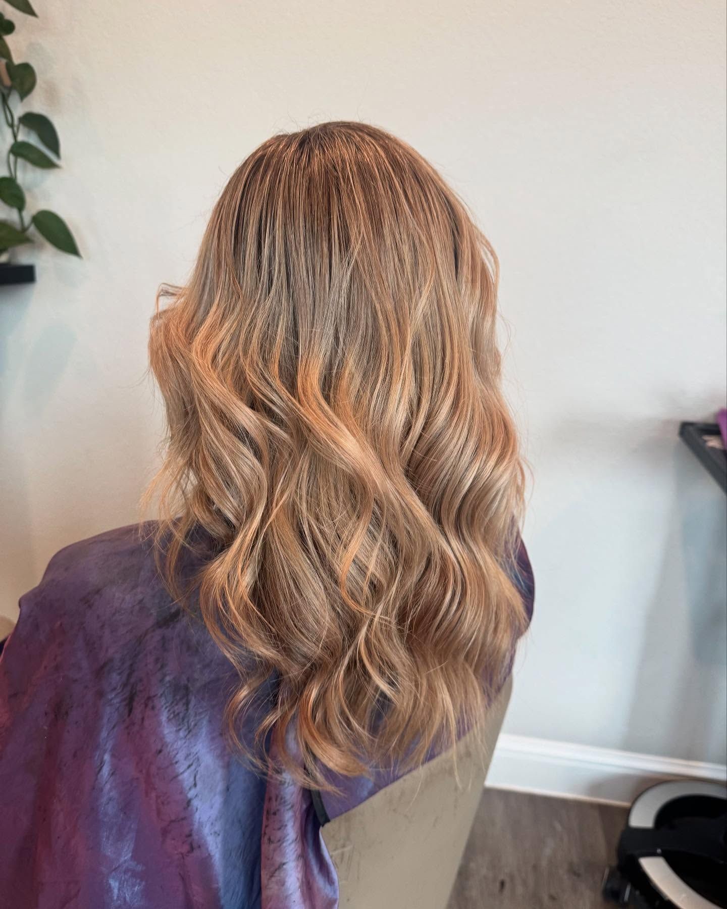 Person with long, wavy, crimped light brown hair, wearing a purple cape in a salon.