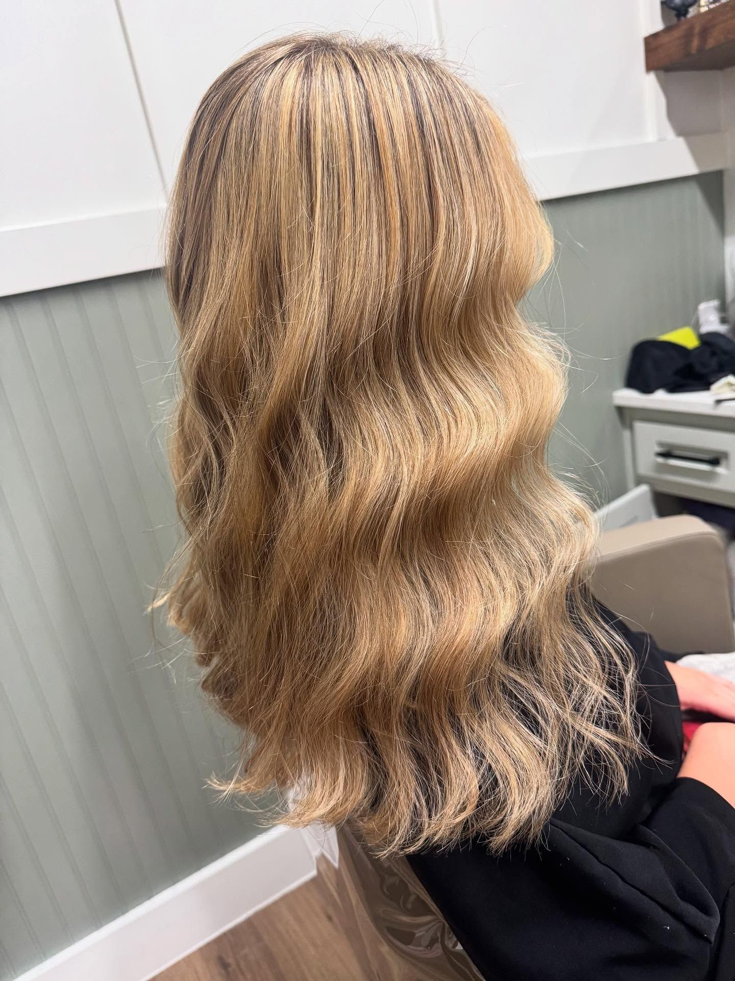 Long wavy blonde hair with dark roots, indoors, illuminated.