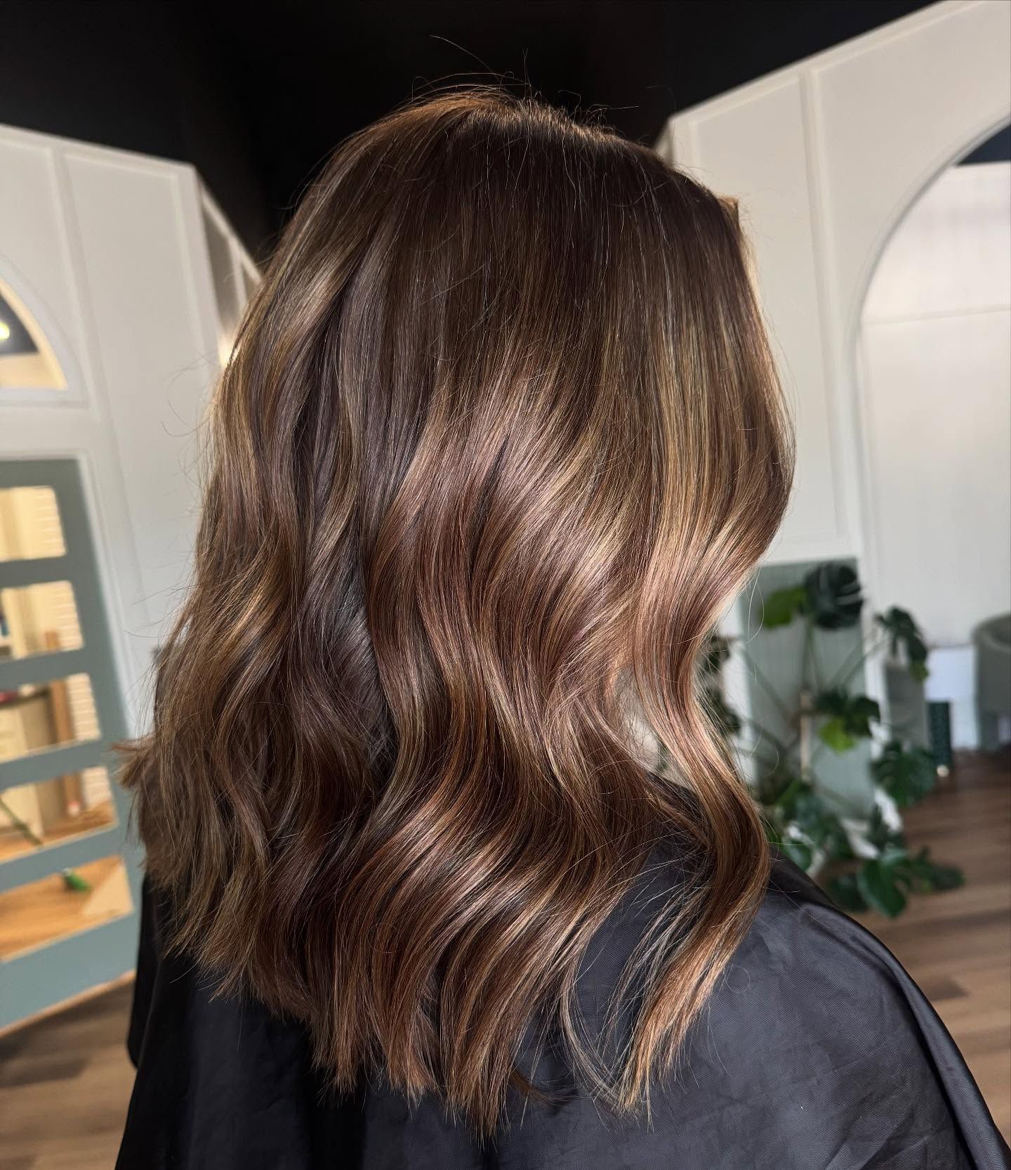 Woman's wavy brown hair with subtle highlights, styled in a salon setting.