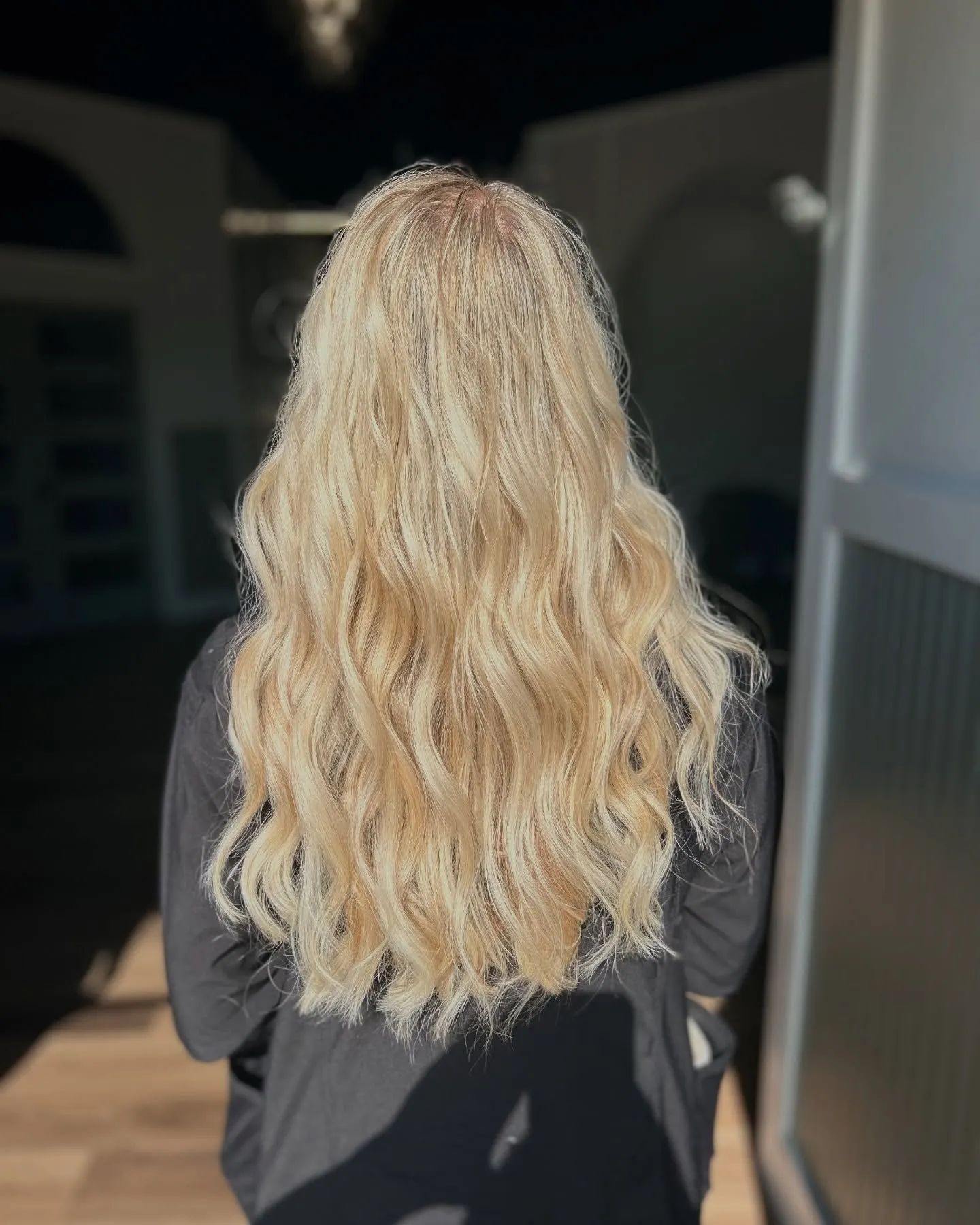 Back view of a person with long wavy blonde hair wearing a black top outdoors