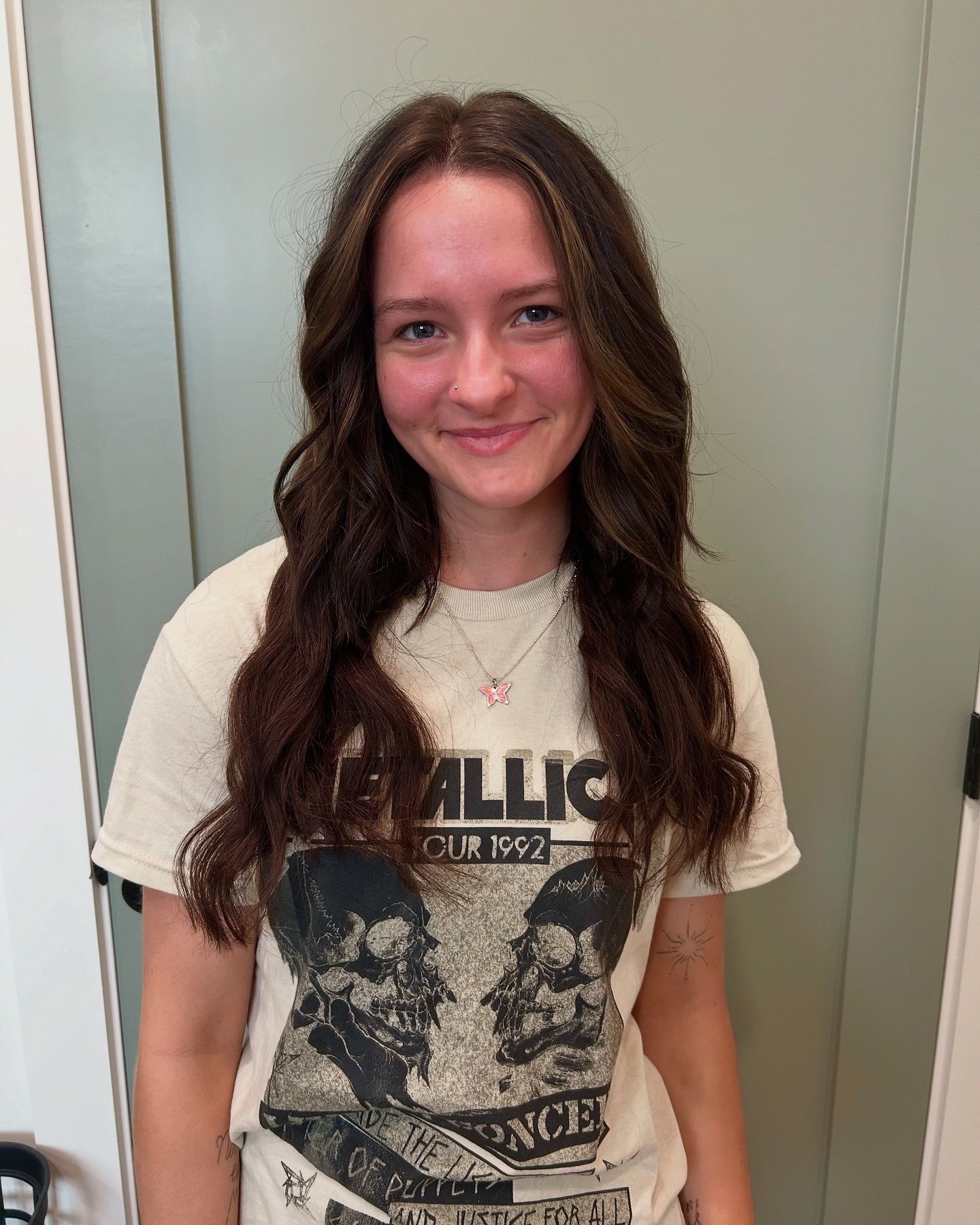 Young person with wavy brown hair, wearing a Metallica t-shirt, smiles at the camera.