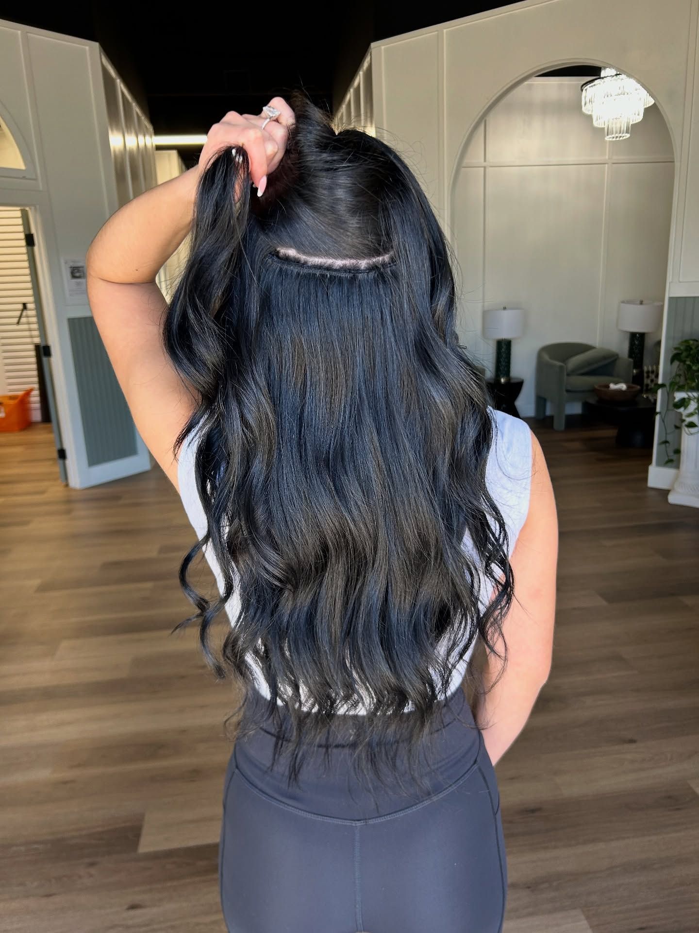 Woman with long black hair, holding some up, in a salon setting.