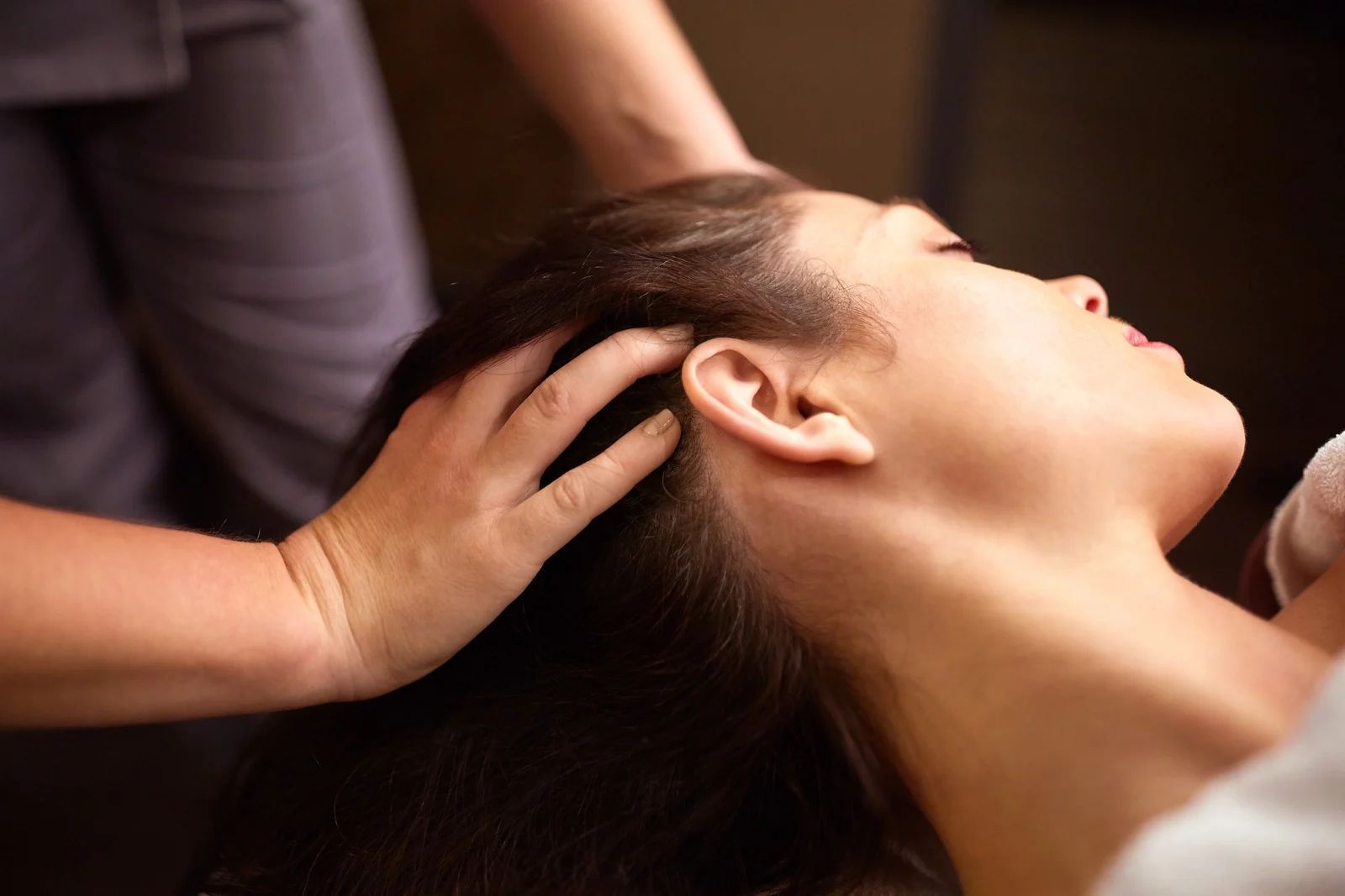 Hands massaging a person’s scalp as they recline, with dark hair and a relaxed profile.