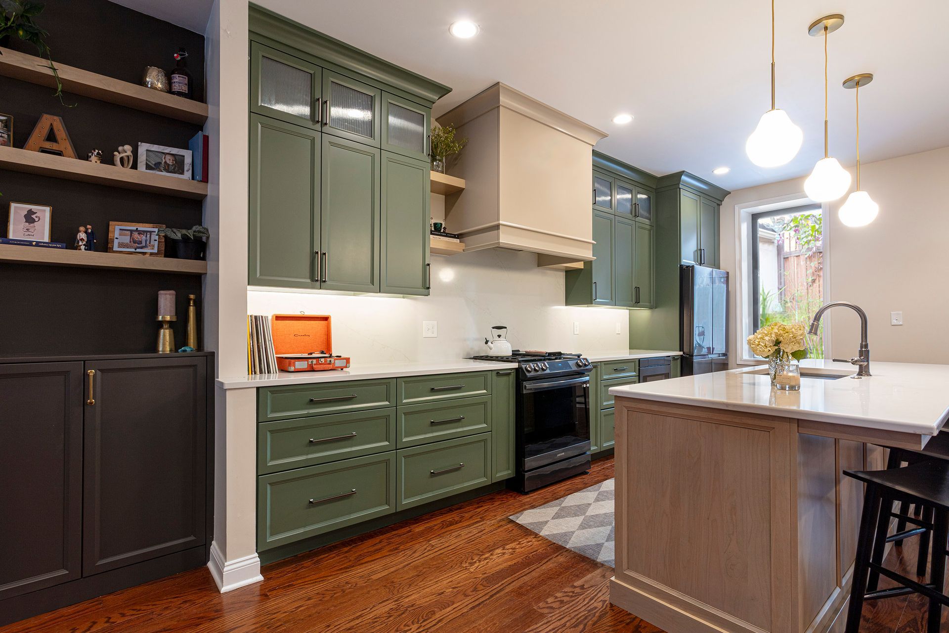 Modern kitchen with olive-green cabinets, wood island, white countertops, and warm pendant lighting.