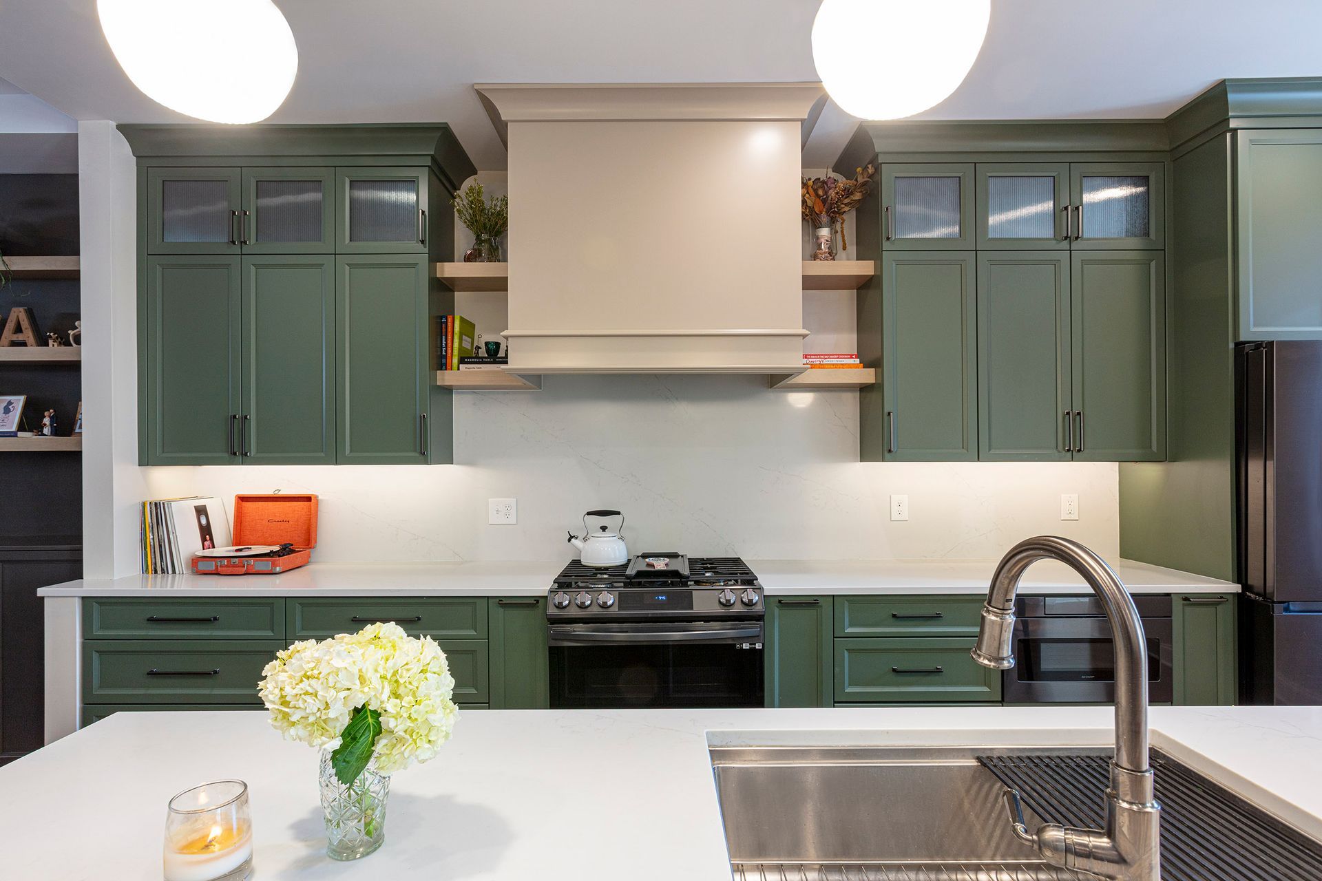 Modern kitchen with green cabinets, white counters, stainless stove, and flowers on the island