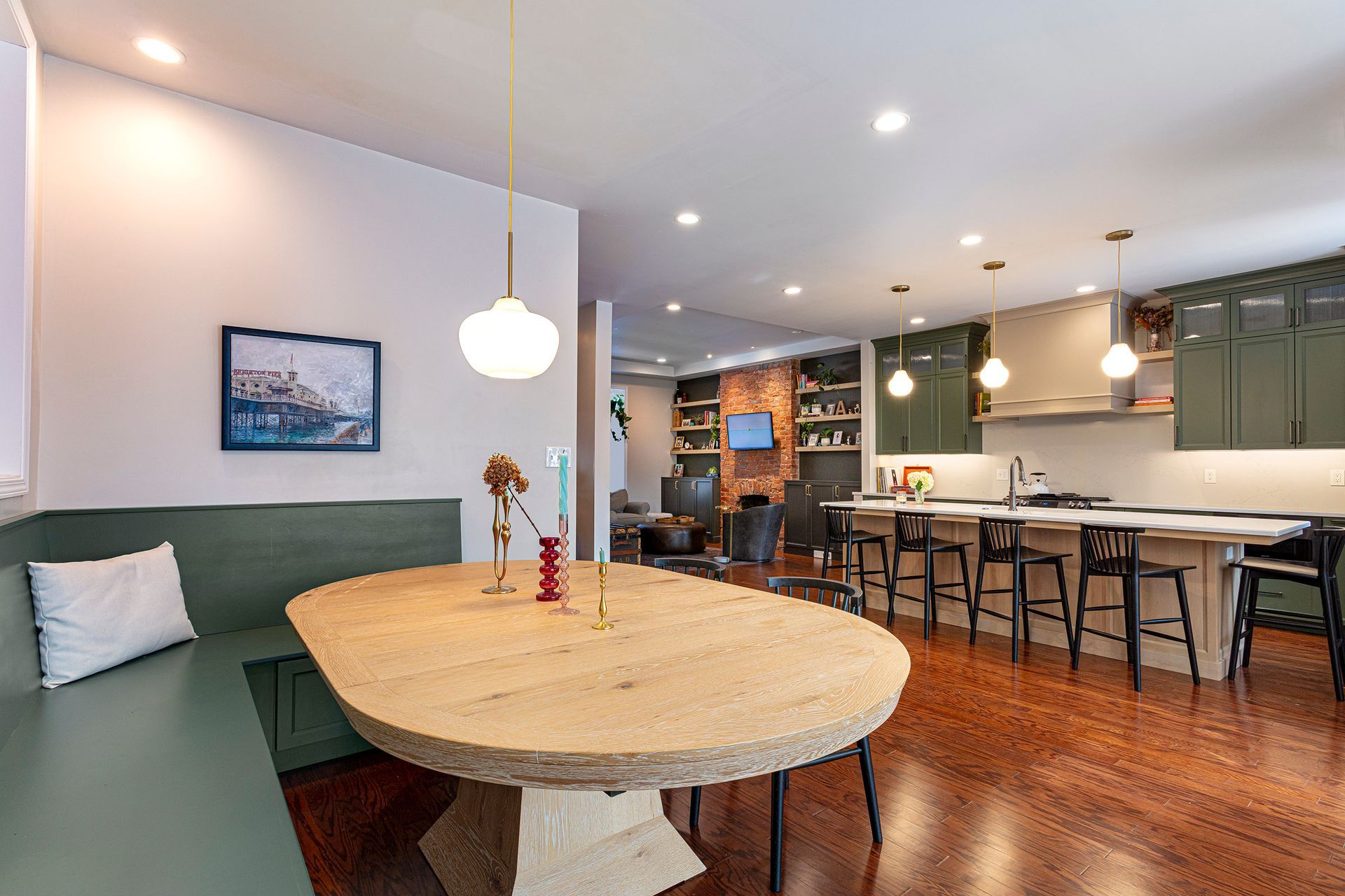 Modern kitchen-dining area with round wood table, green banquette, and pendant lights over a breakfast bar