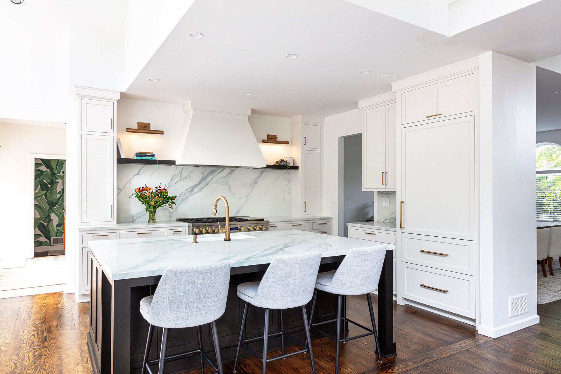 Bright modern kitchen with white island, marble backsplash, black stools, and built-in cabinets