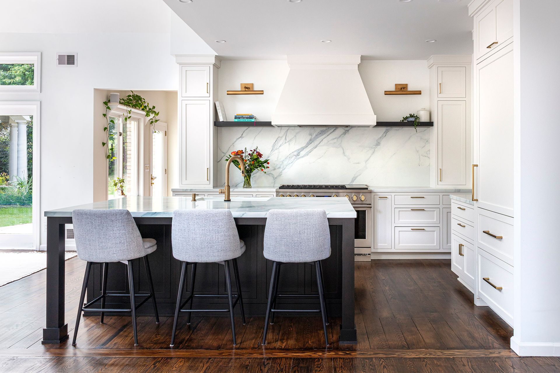 Bright modern kitchen with white cabinets, marble backsplash, island, and four gray stools on dark wood floors