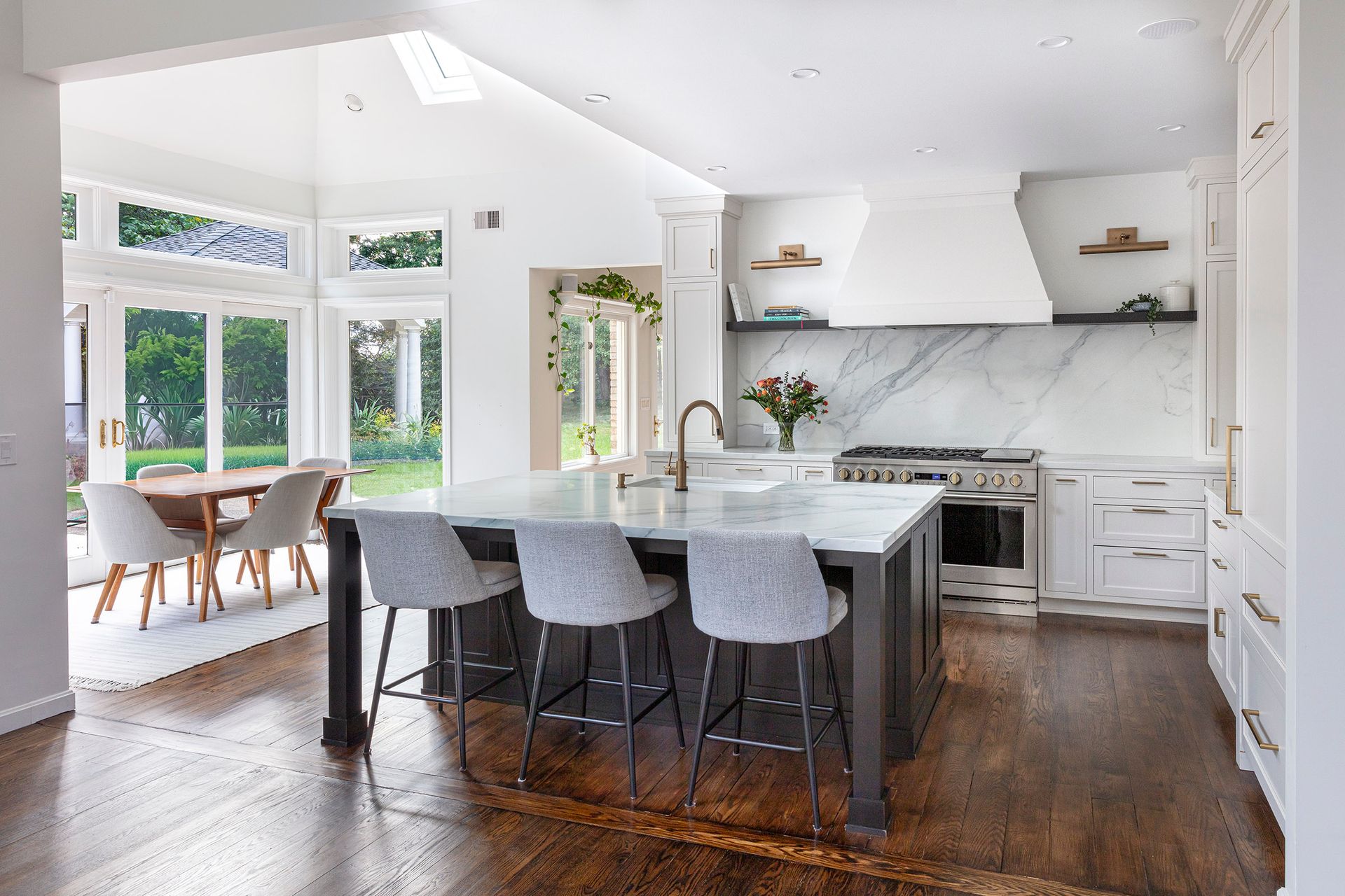 Bright open kitchen with white cabinets, marble island, gray stools, and dining area by large windows