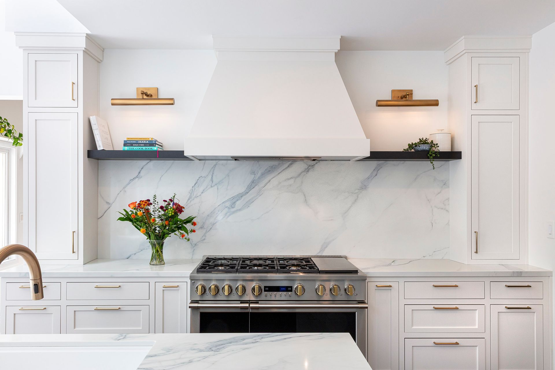 Bright white kitchen with marble backsplash, stainless range, open shelves, and a vase of flowers