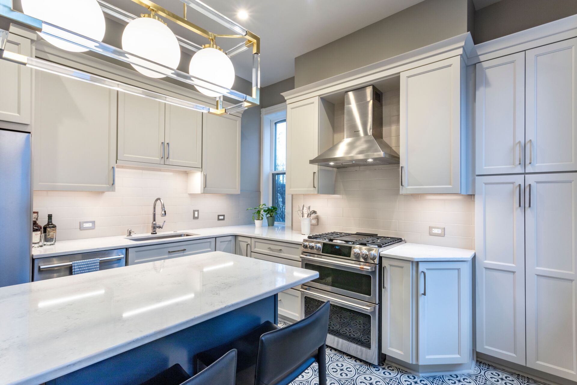 Bright modern kitchen with white cabinets, blue accents, marble island, and stainless steel stove