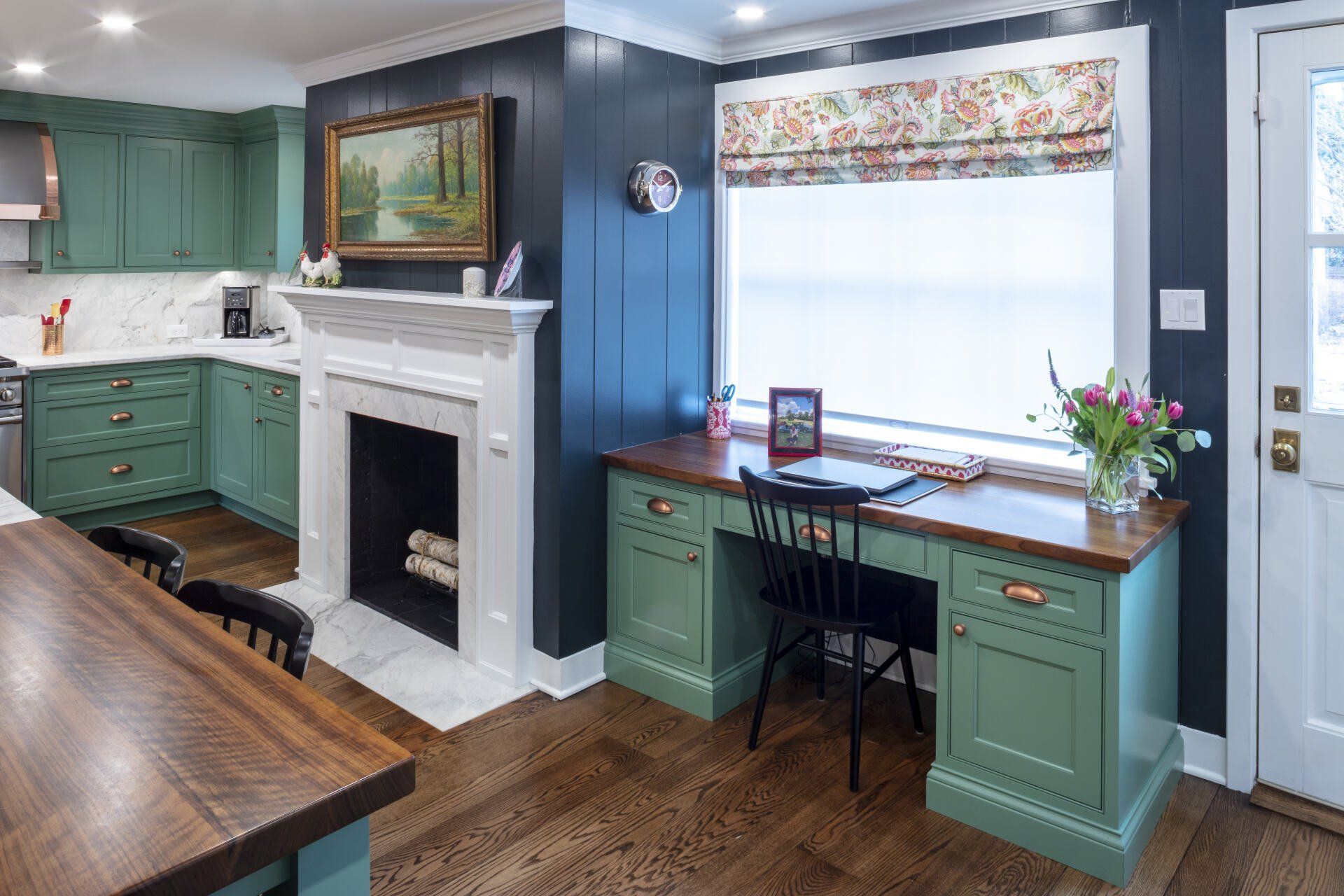 Cozy kitchen with green cabinets, white fireplace, and a blue desk under a window seat.