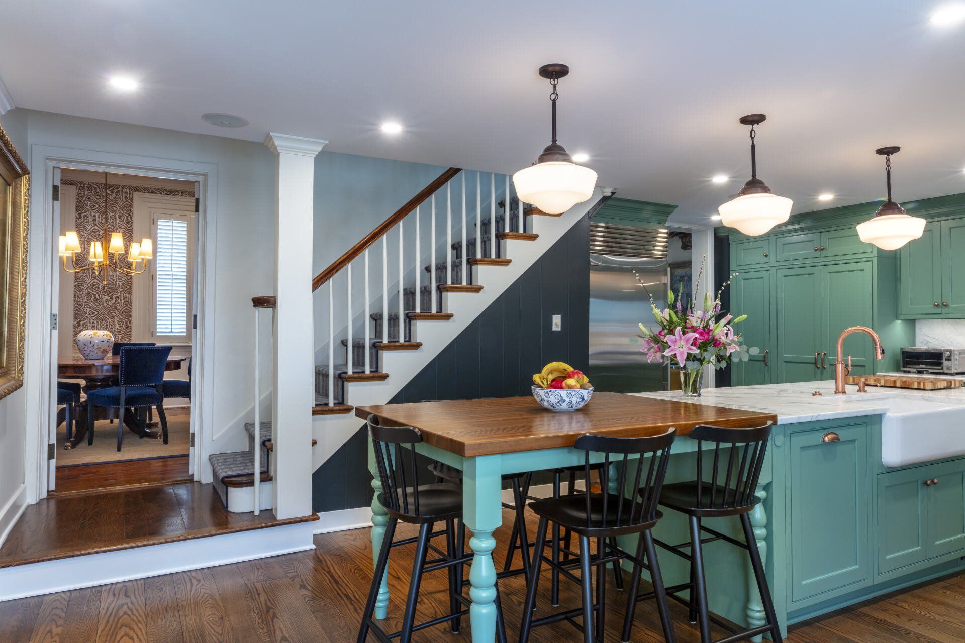 Open kitchen with teal island, staircase, pendant lights, and adjoining dining room